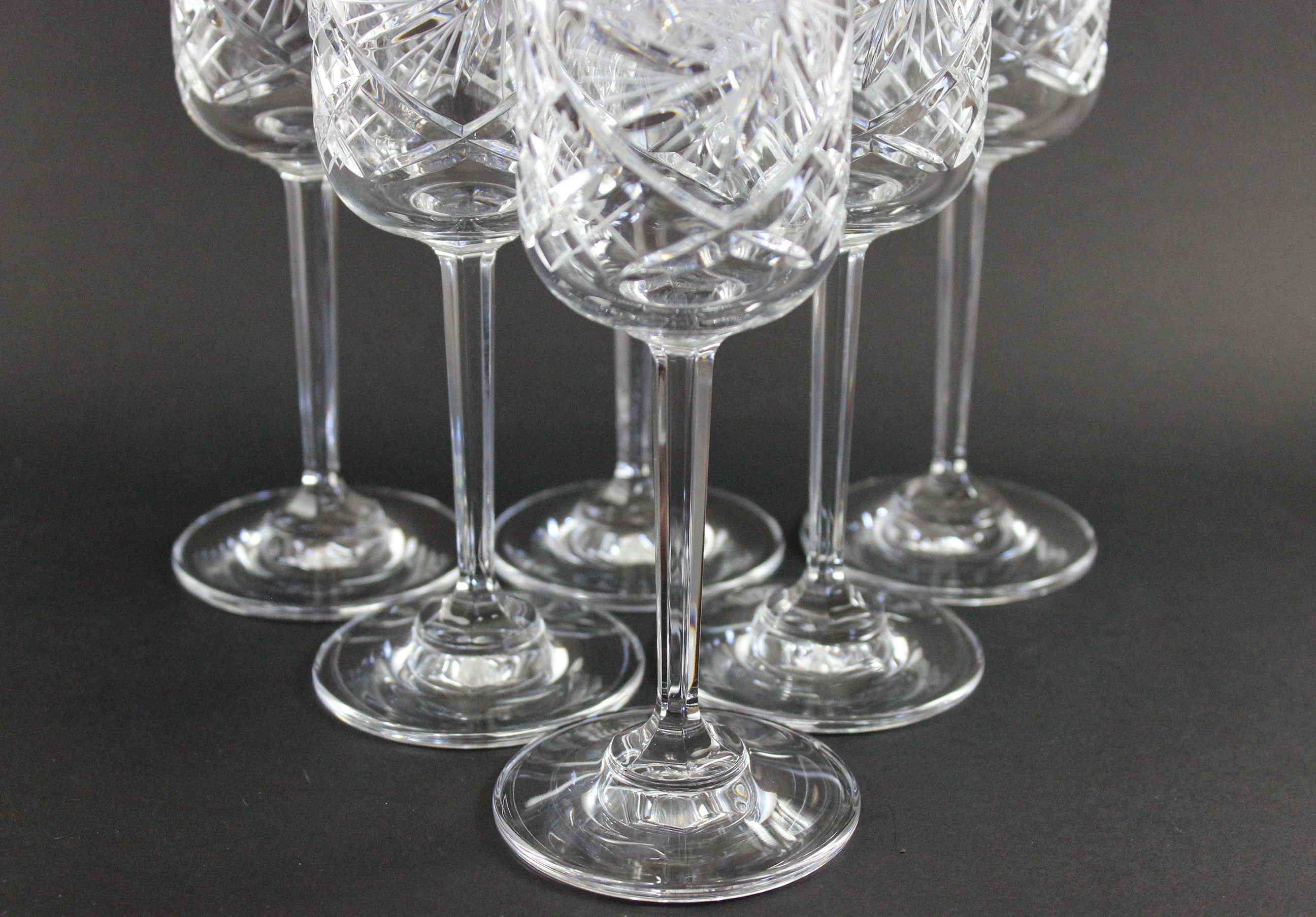 Set of six crystal champagne flutes with cut designs on a black background