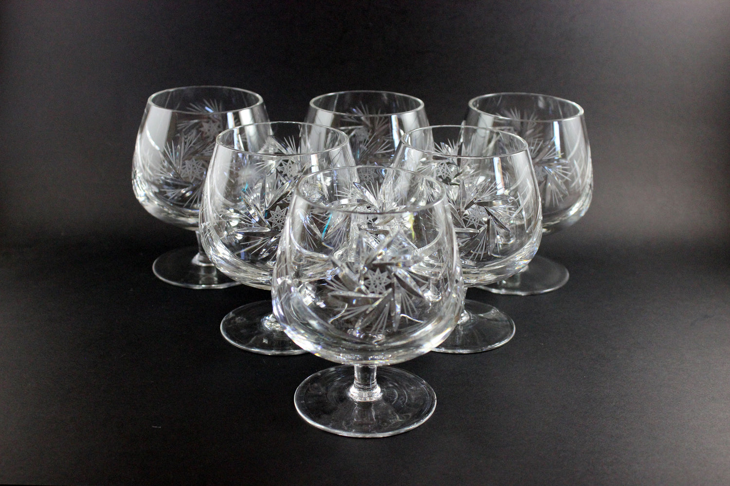 Set of six crystal glasses with intricate designs on a black background