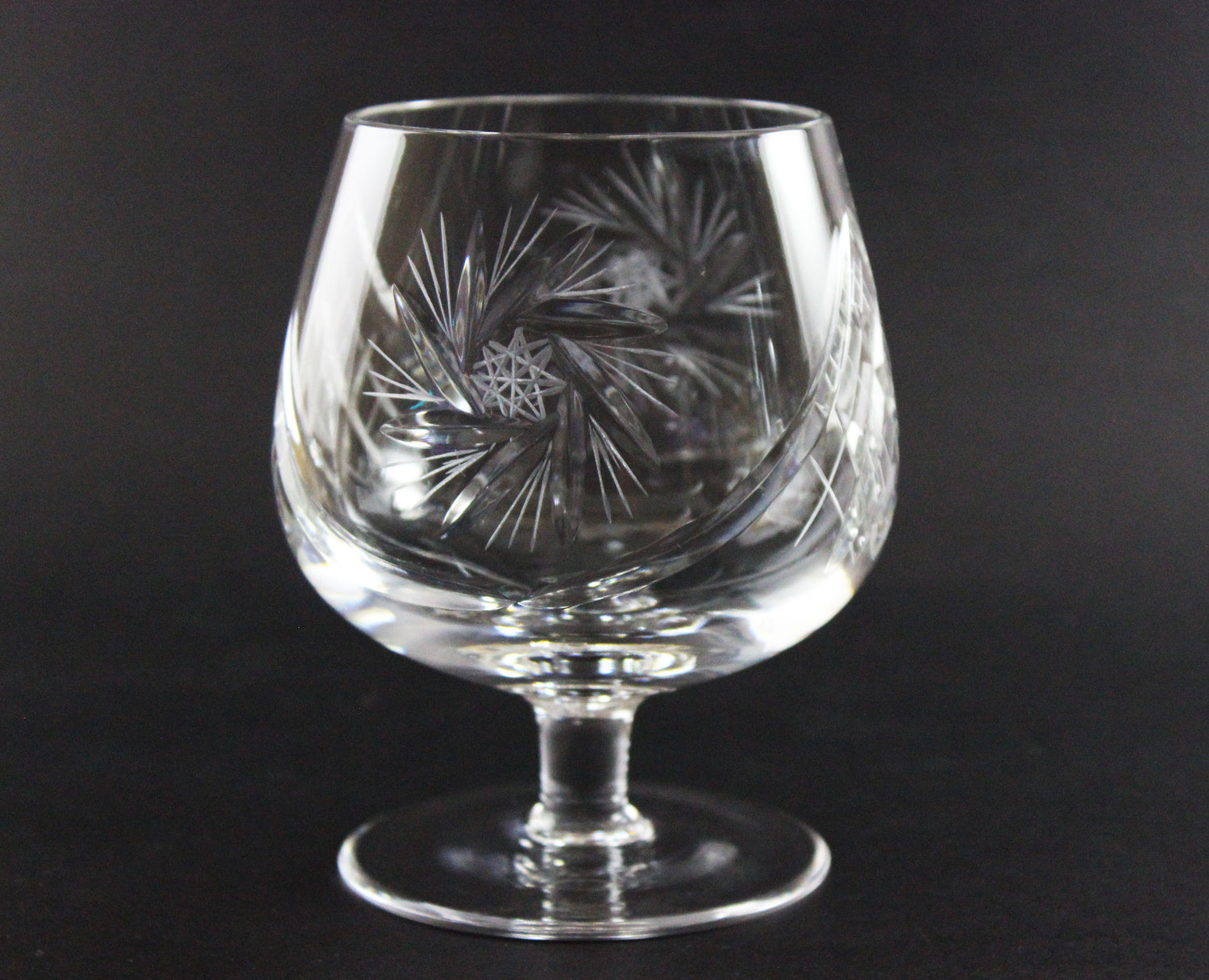 Clear glass snifter with intricate etching on a black background