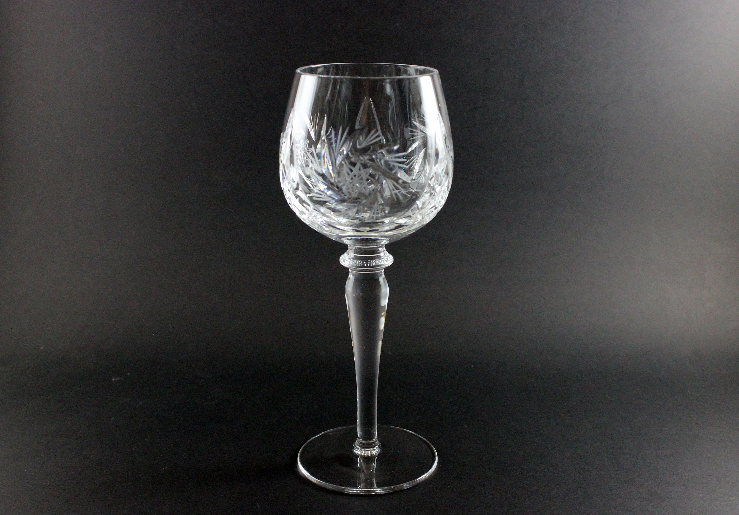 Clear glass wine goblet with intricate design on a black background