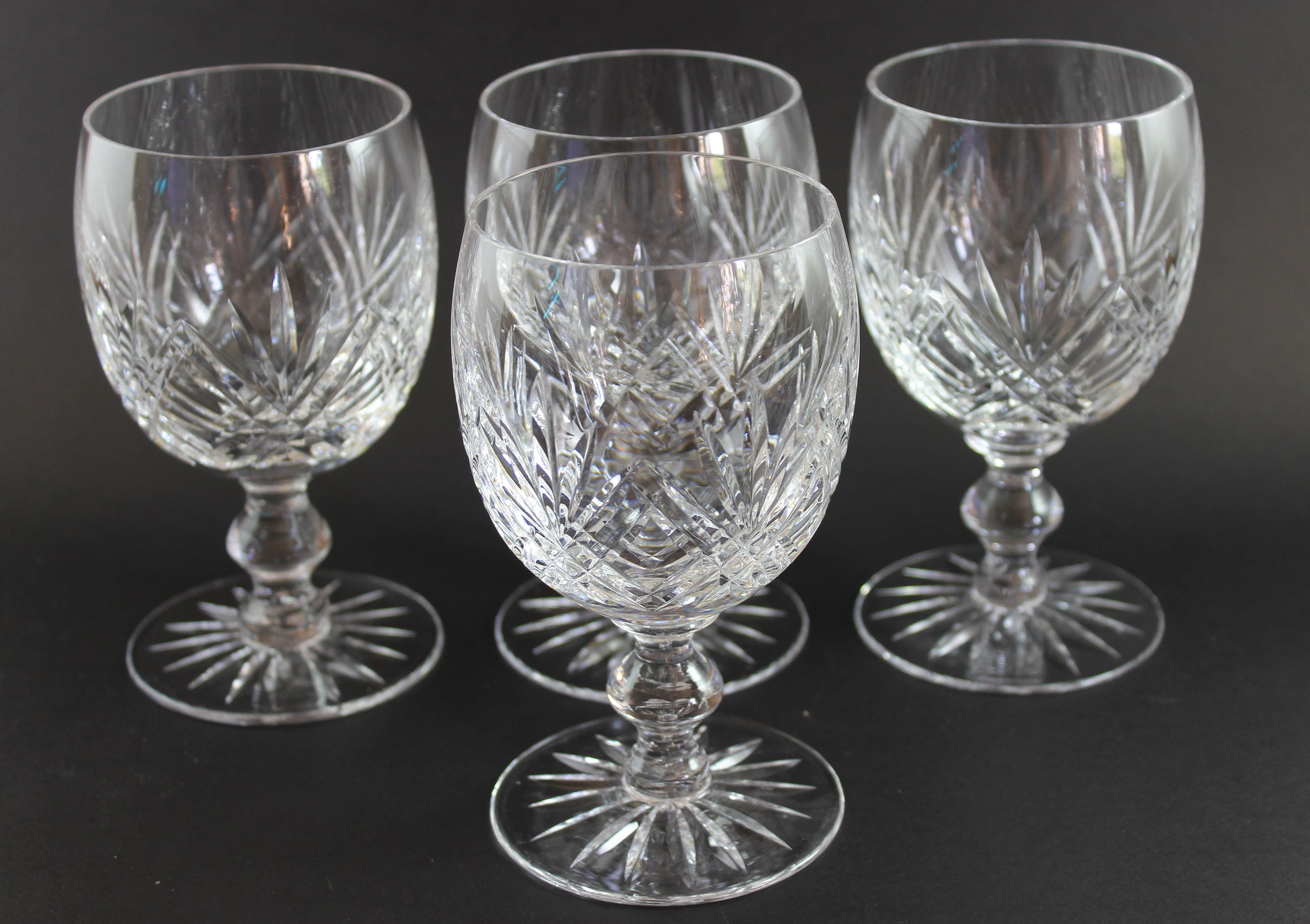 Set of four crystal glasses with cut patterns on a dark background
