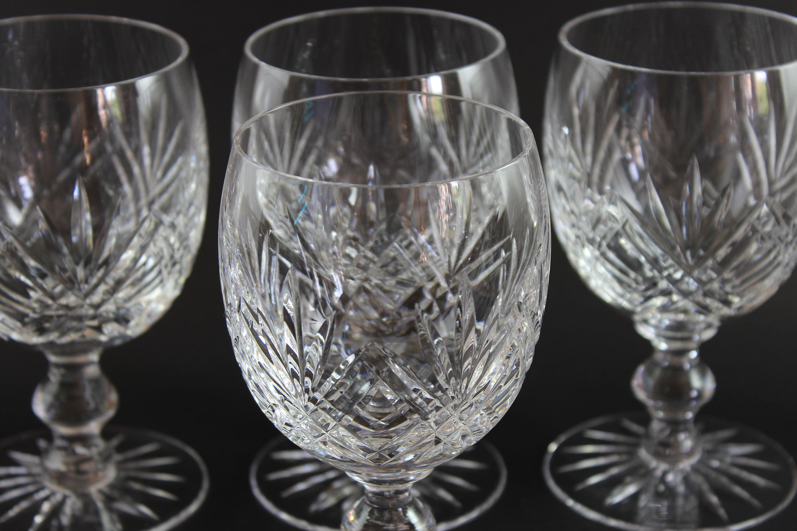 Set of four crystal wine glasses with intricate cut patterns on a black background