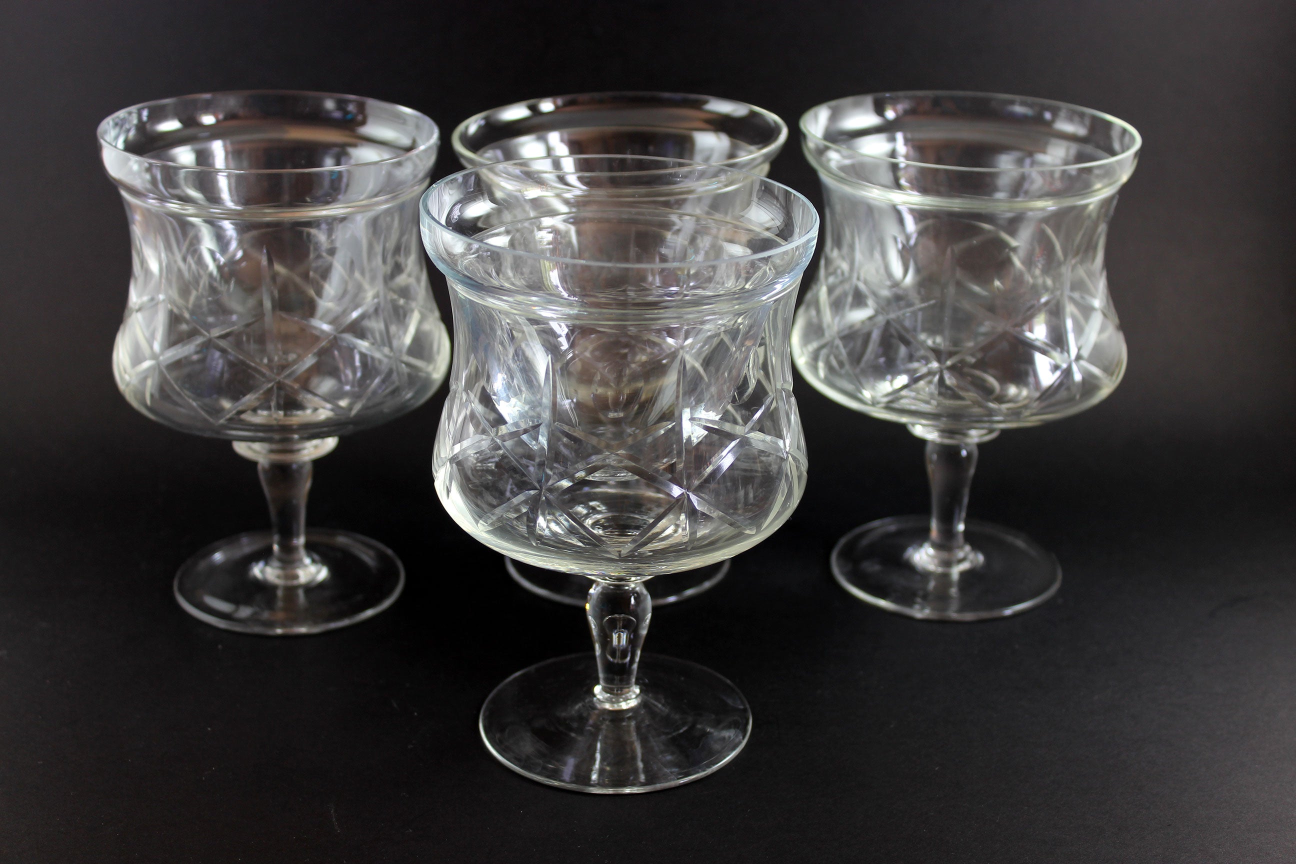 Four clear glass goblets with textured design on a black background