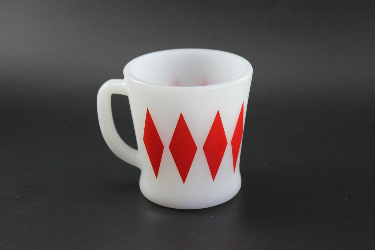 A white glass coffee mug with a red harlequin diamond pattern, set against a dark gray background.