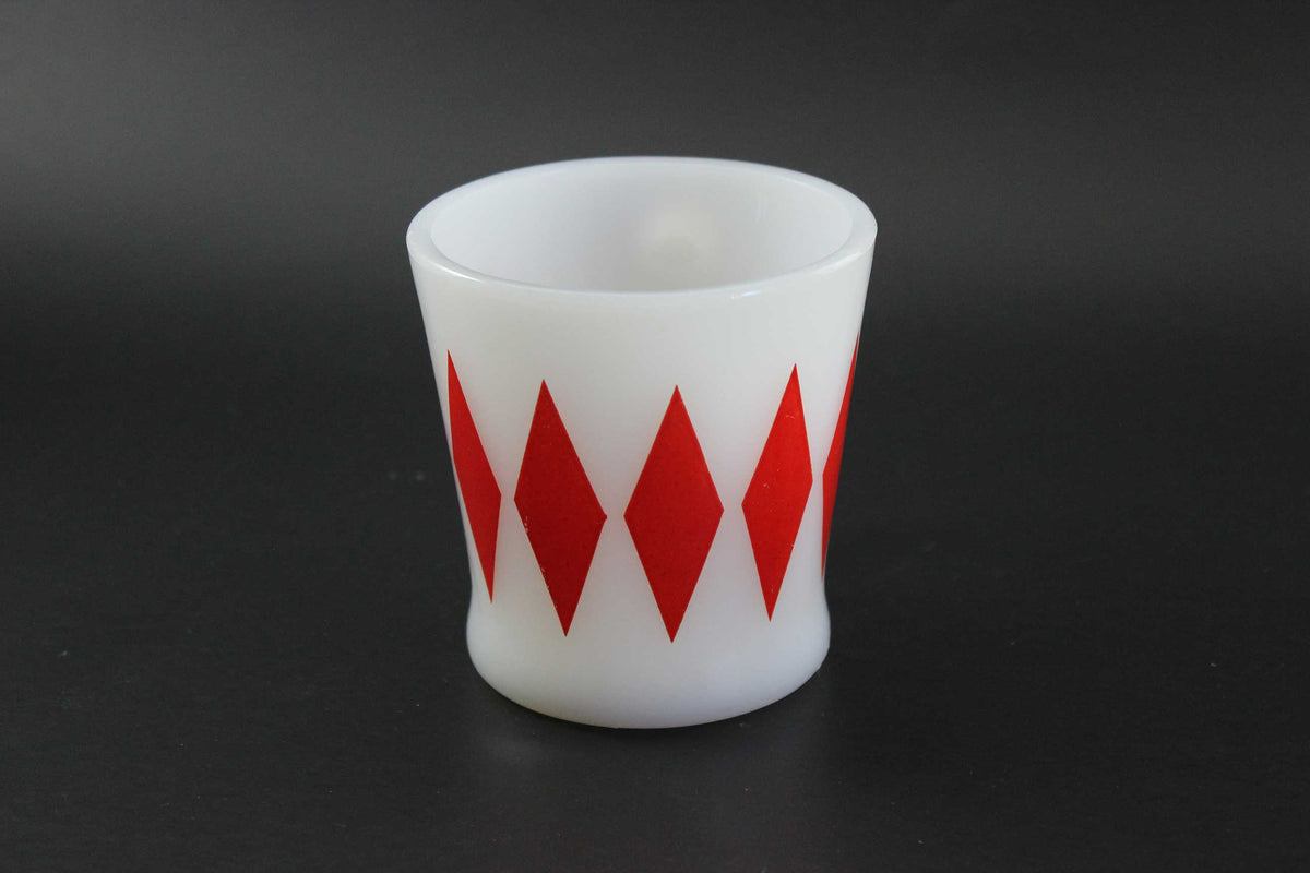 A white glass coffee mug with a red harlequin diamond pattern, set against a dark gray background.
