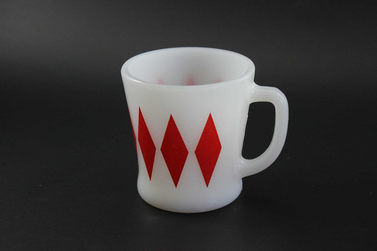 A white glass coffee mug with a red harlequin diamond pattern, set against a dark gray background.