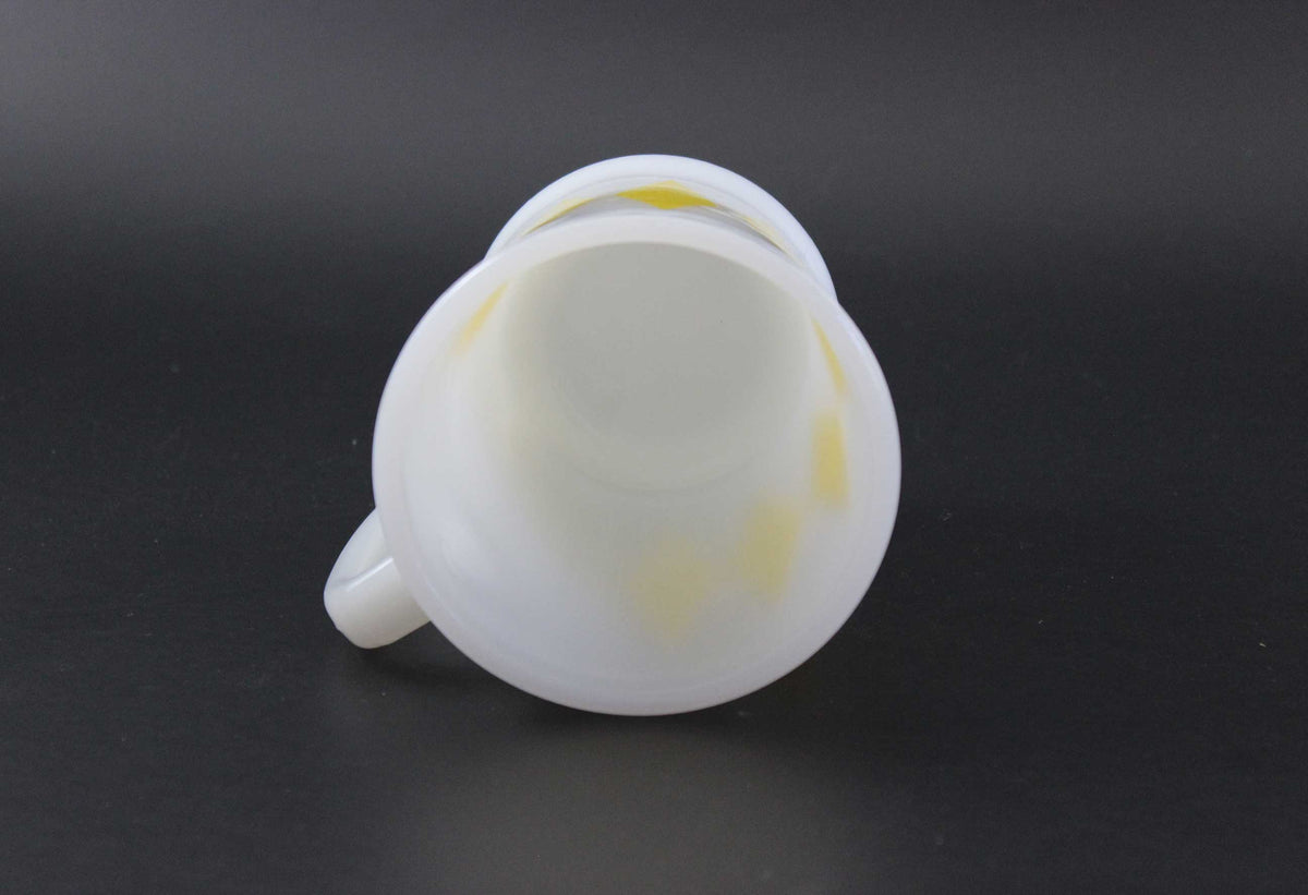 A white glass coffee mug with a yellow harlequin diamond pattern, set against a dark gray background.
