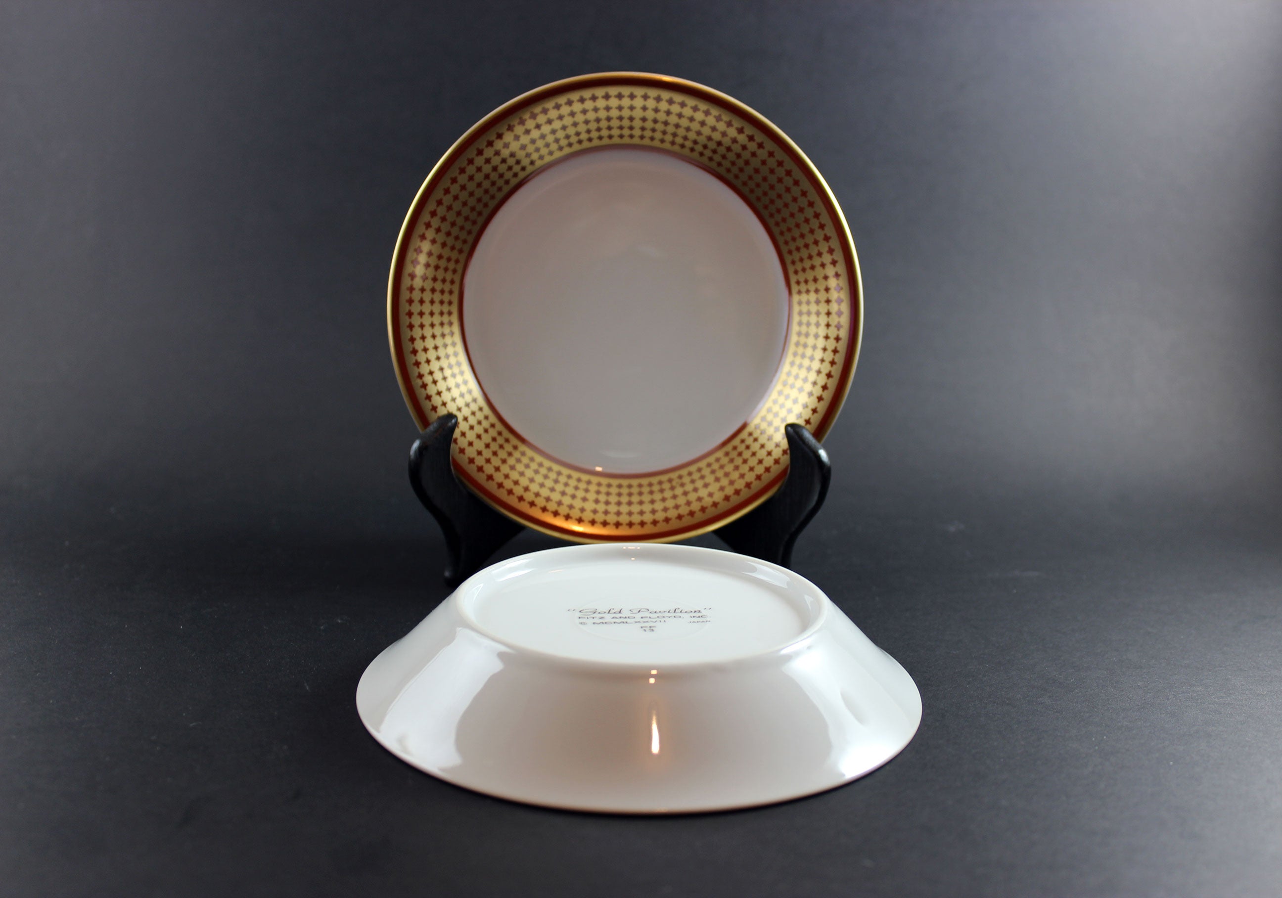 Two ceramic fruit nappies with gold rims on a dark background