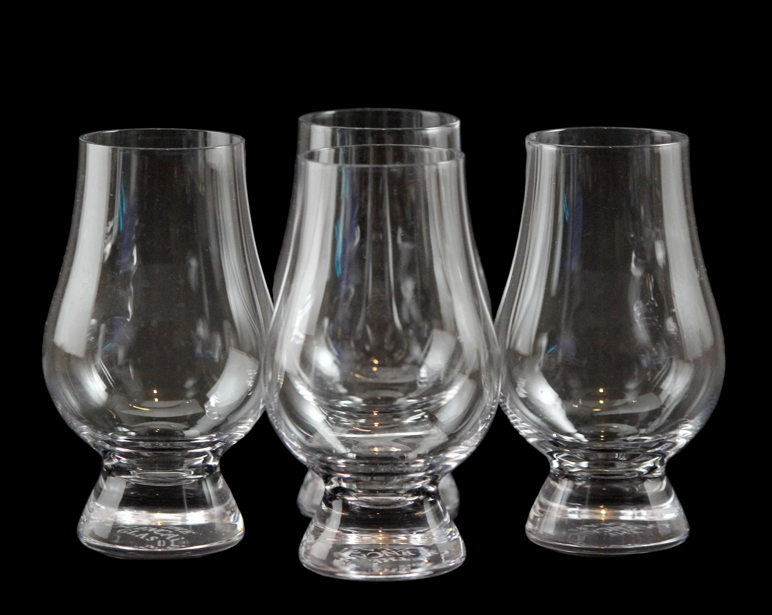 Four clear glass whisky glasses on a black background