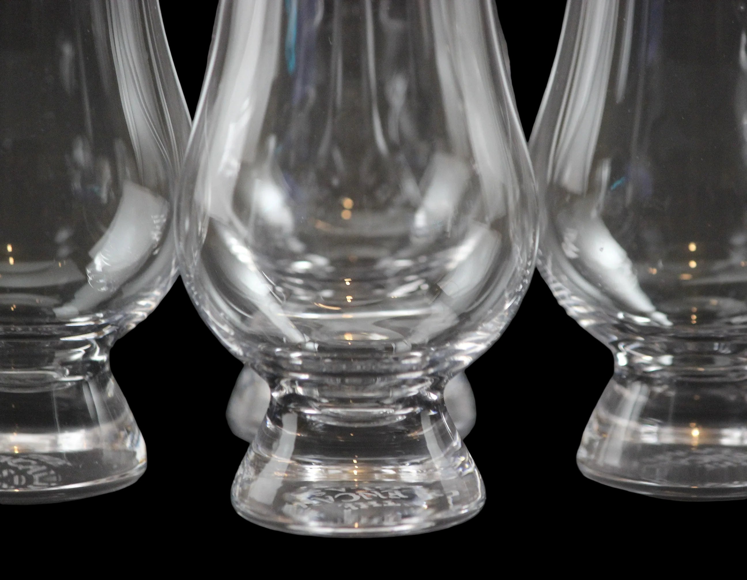 Closeup of four clear glass whisky glasses on a black background
