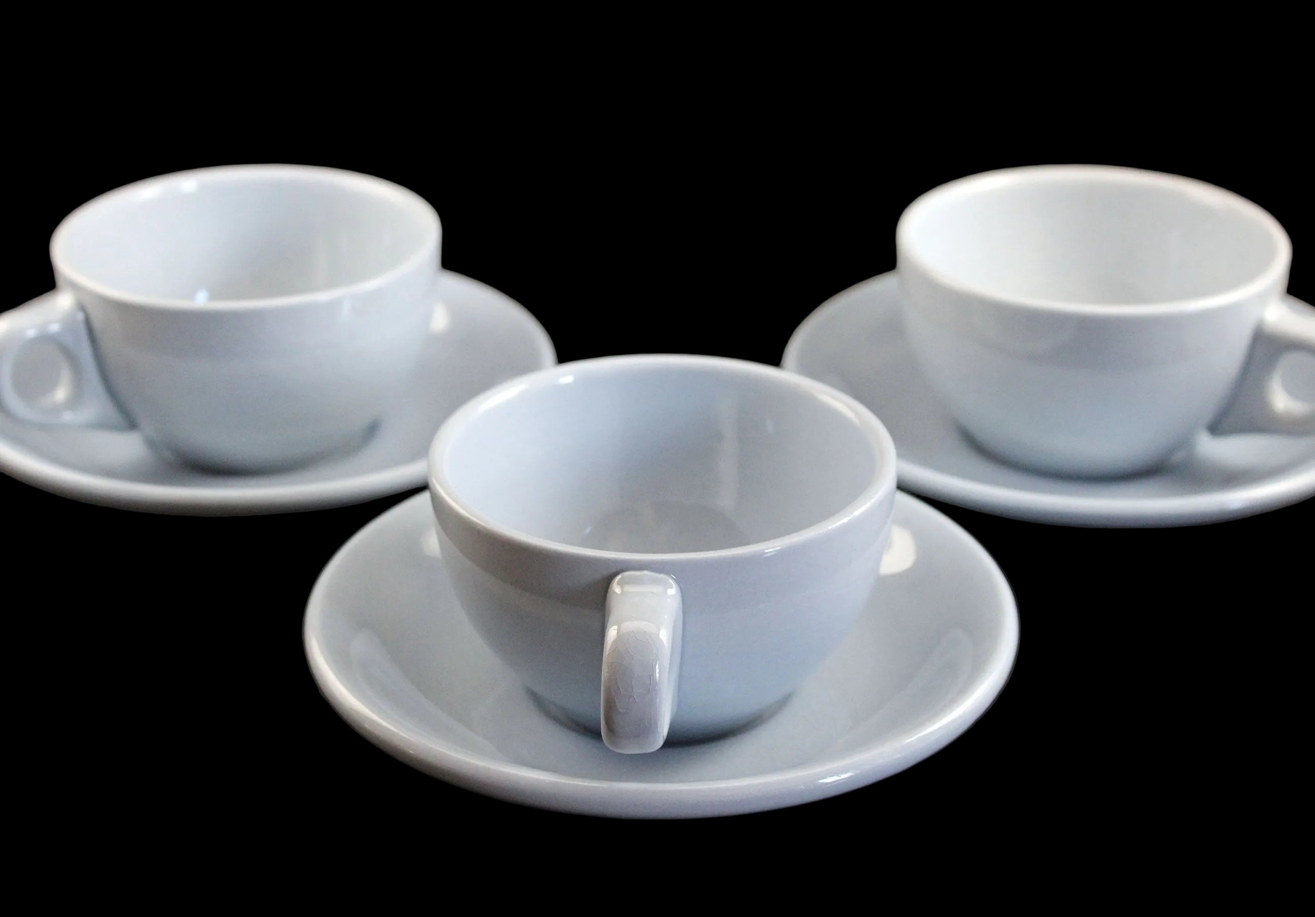 Three blue ceramic cups with saucers on a dark surface