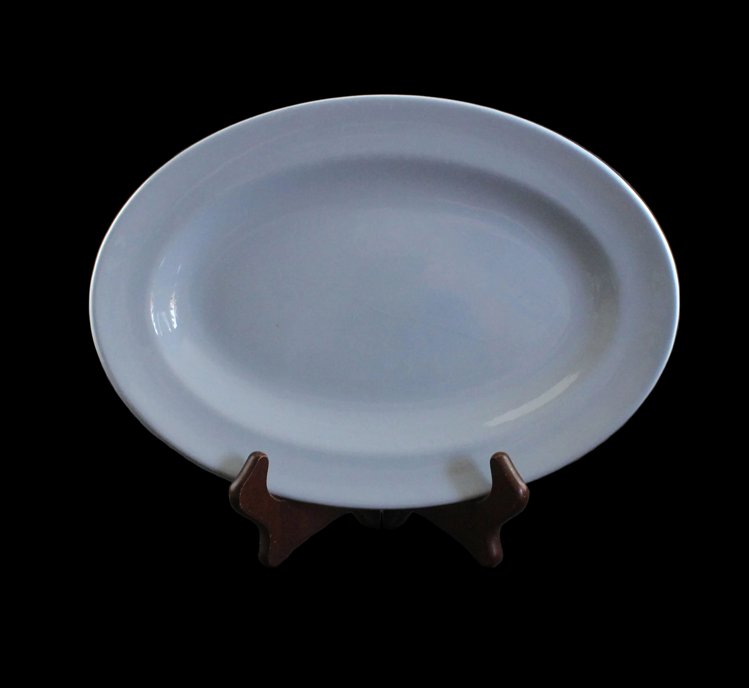 An oval blue ceramic serving platter displayed on a small dark brown wooden stand against a dark gray studio background.