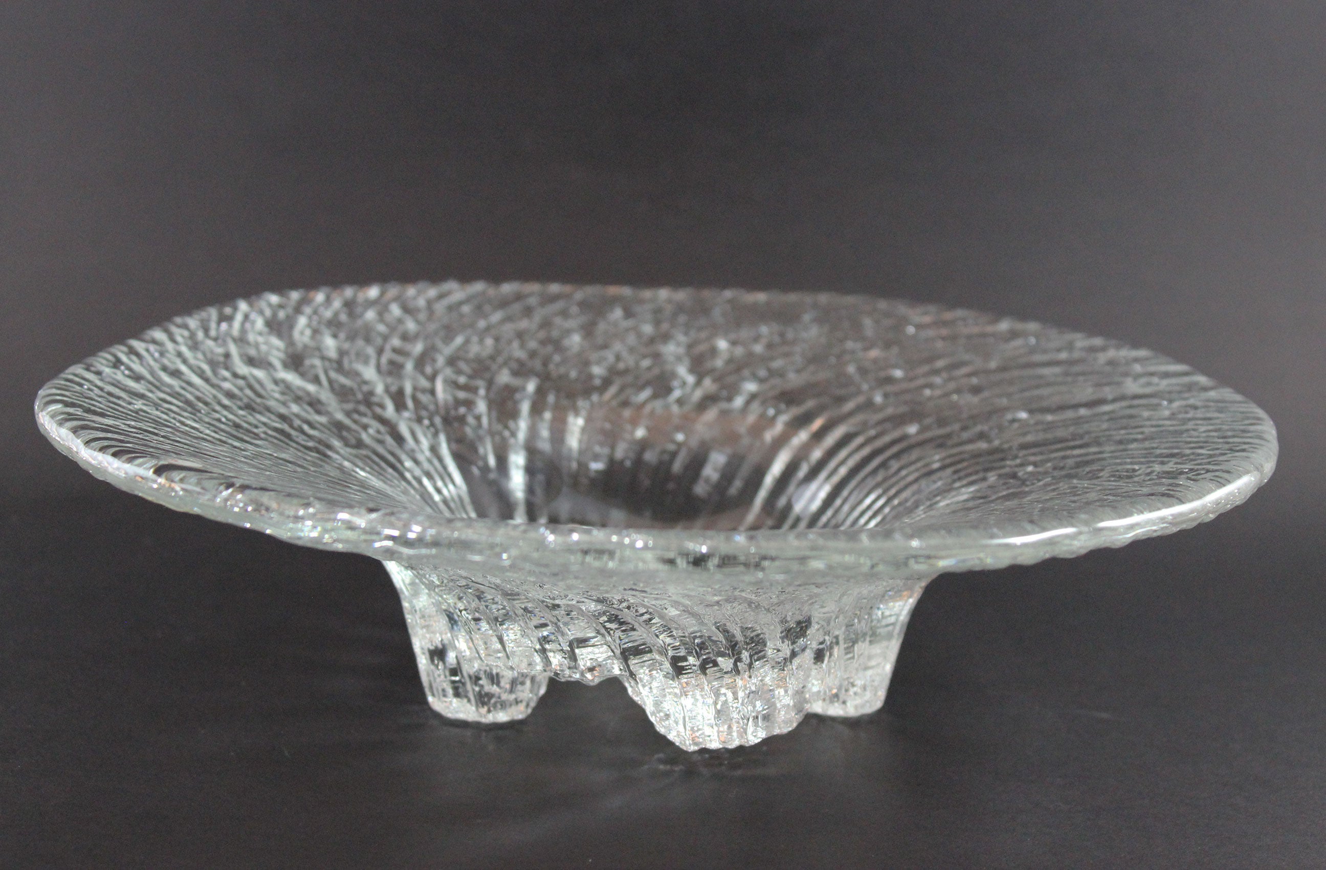 Clear glass footed bowl with textured surface on a dark background