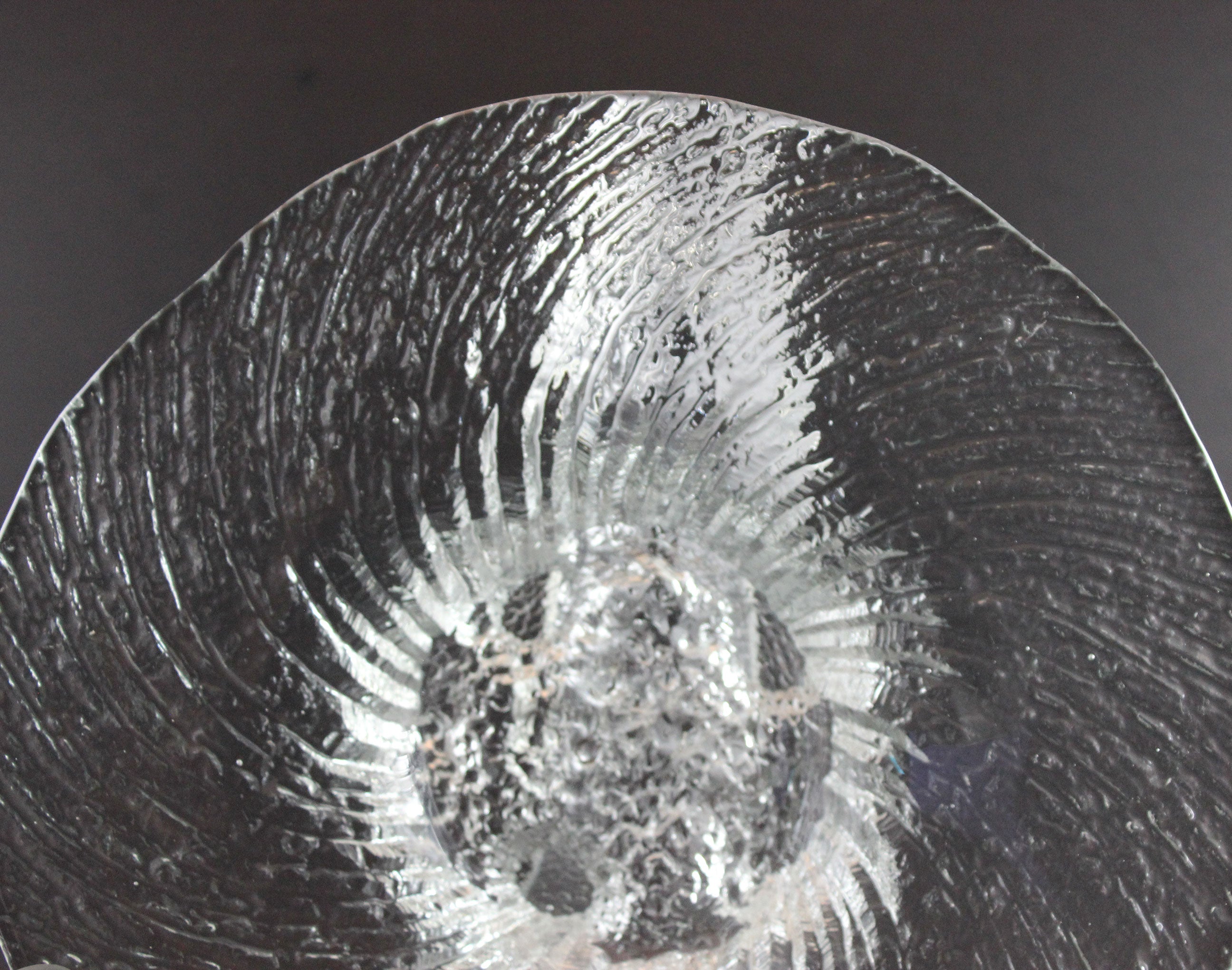Clear glass footed bowl with textured surface on a dark background