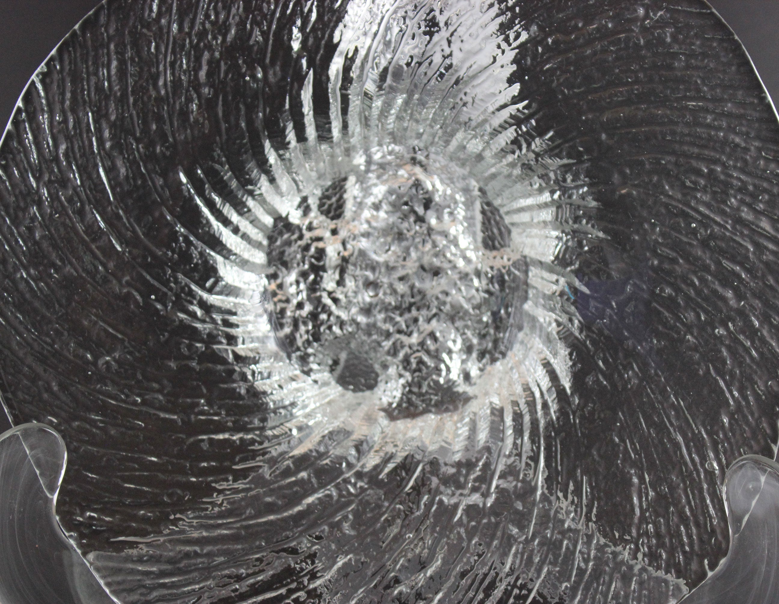 Clear glass footed bowl with textured surface on a dark background