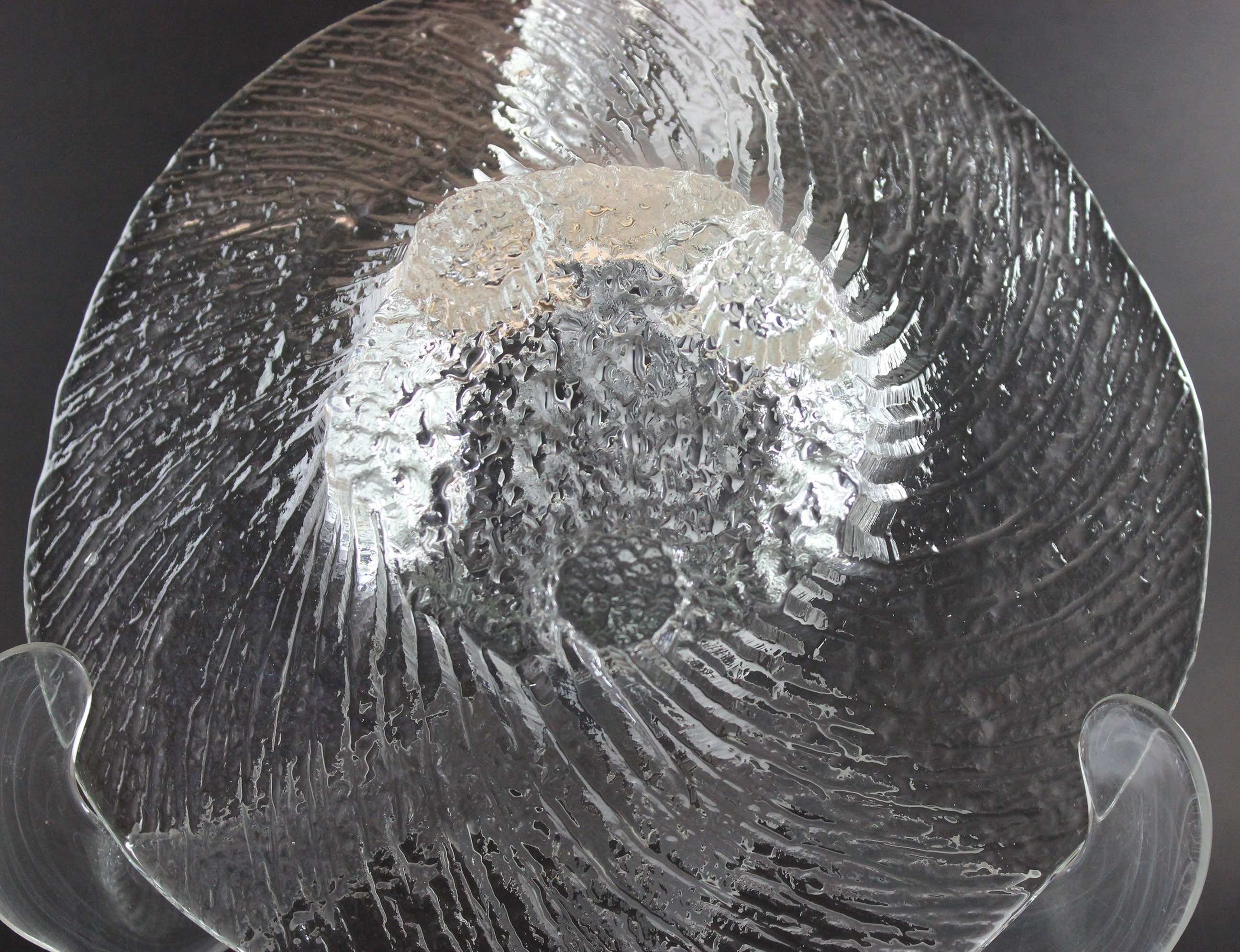 Clear glass footed bowl with textured surface on a dark background