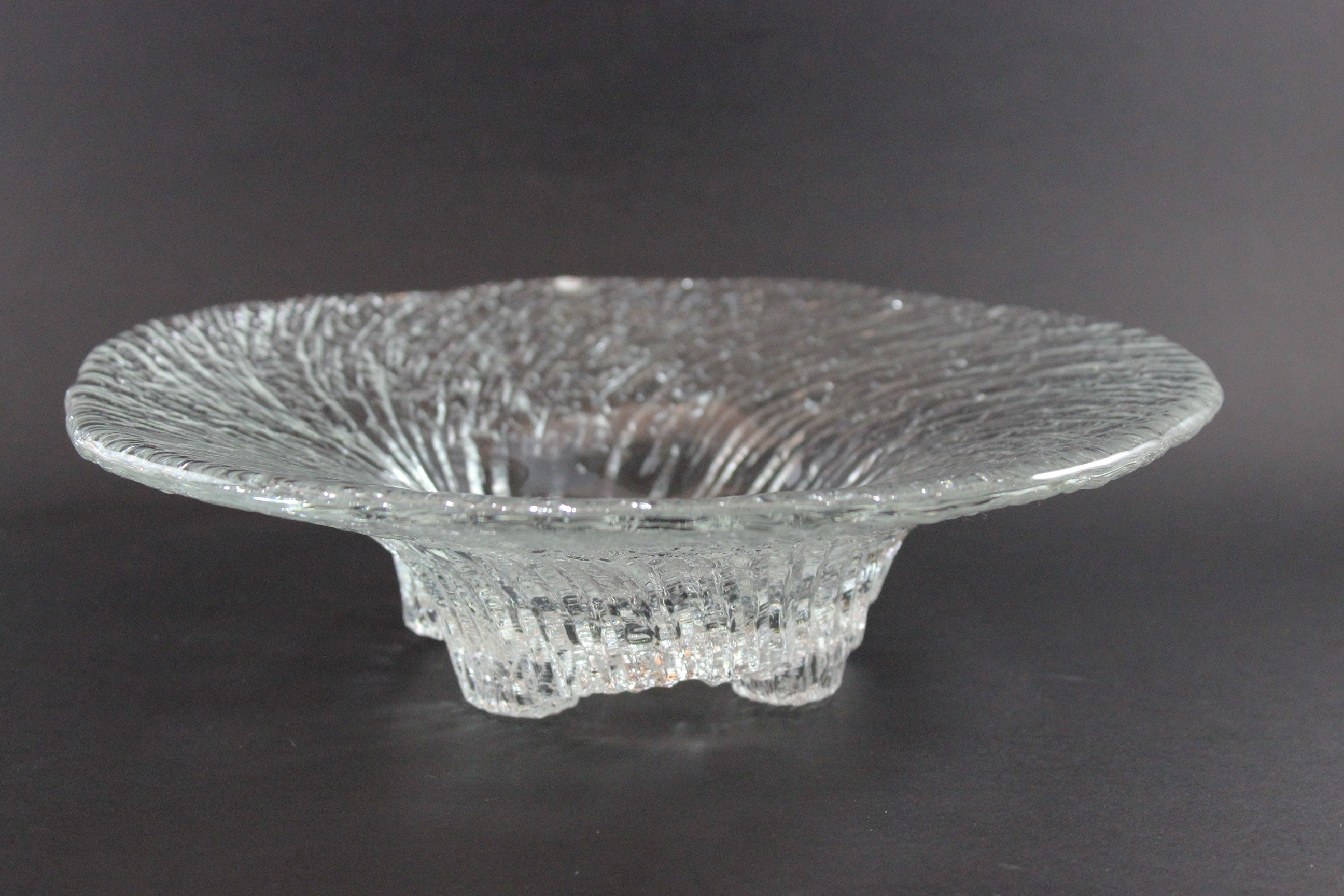 Clear glass footed bowl with textured surface on a dark background