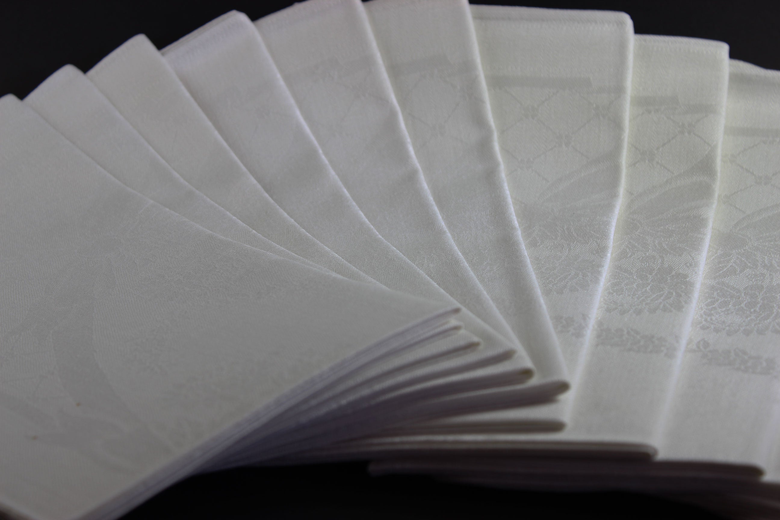 Twelve white damask Irish linen napkins on black background.
