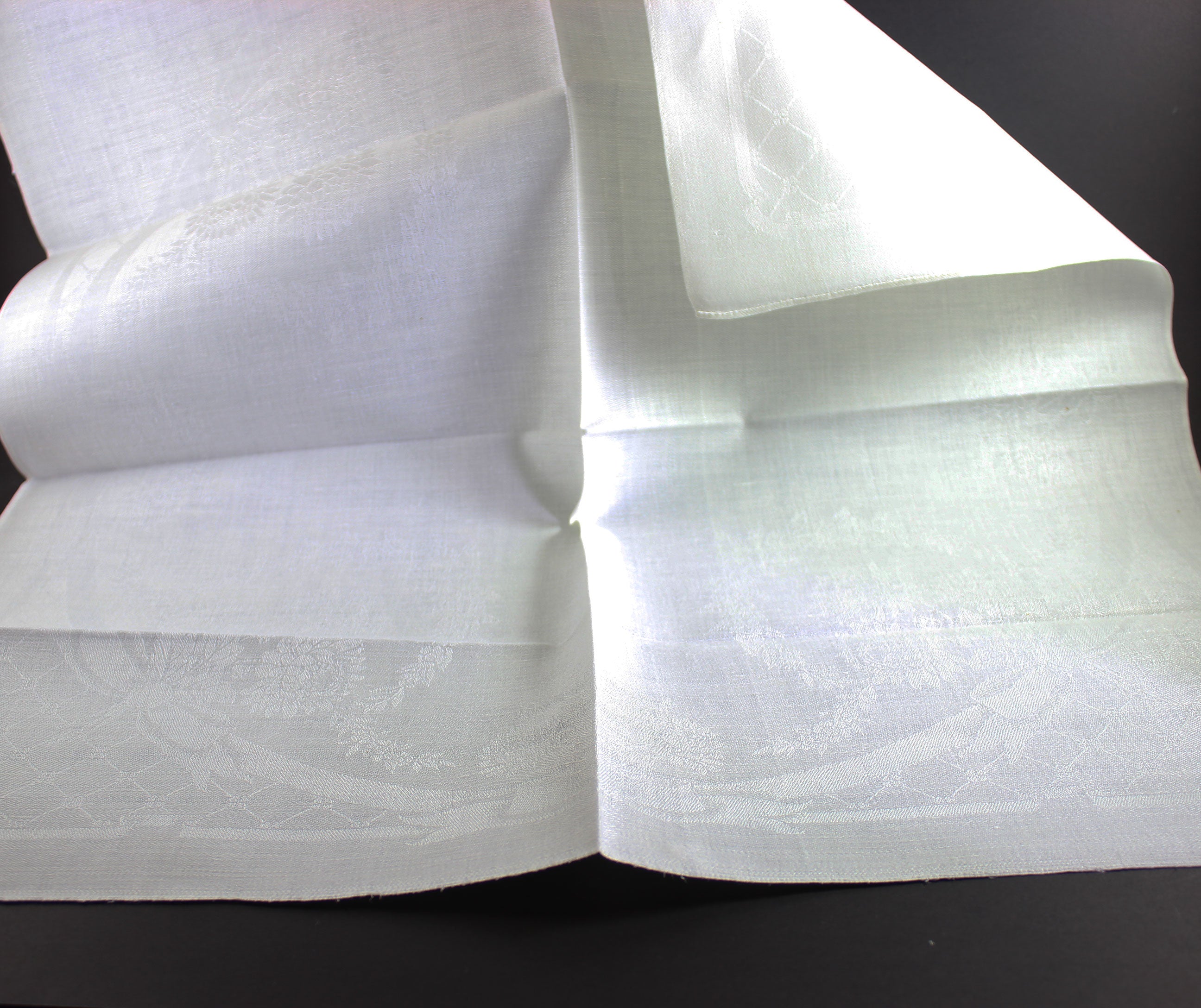 Unfolded white damask Irish linen napkin on black background.