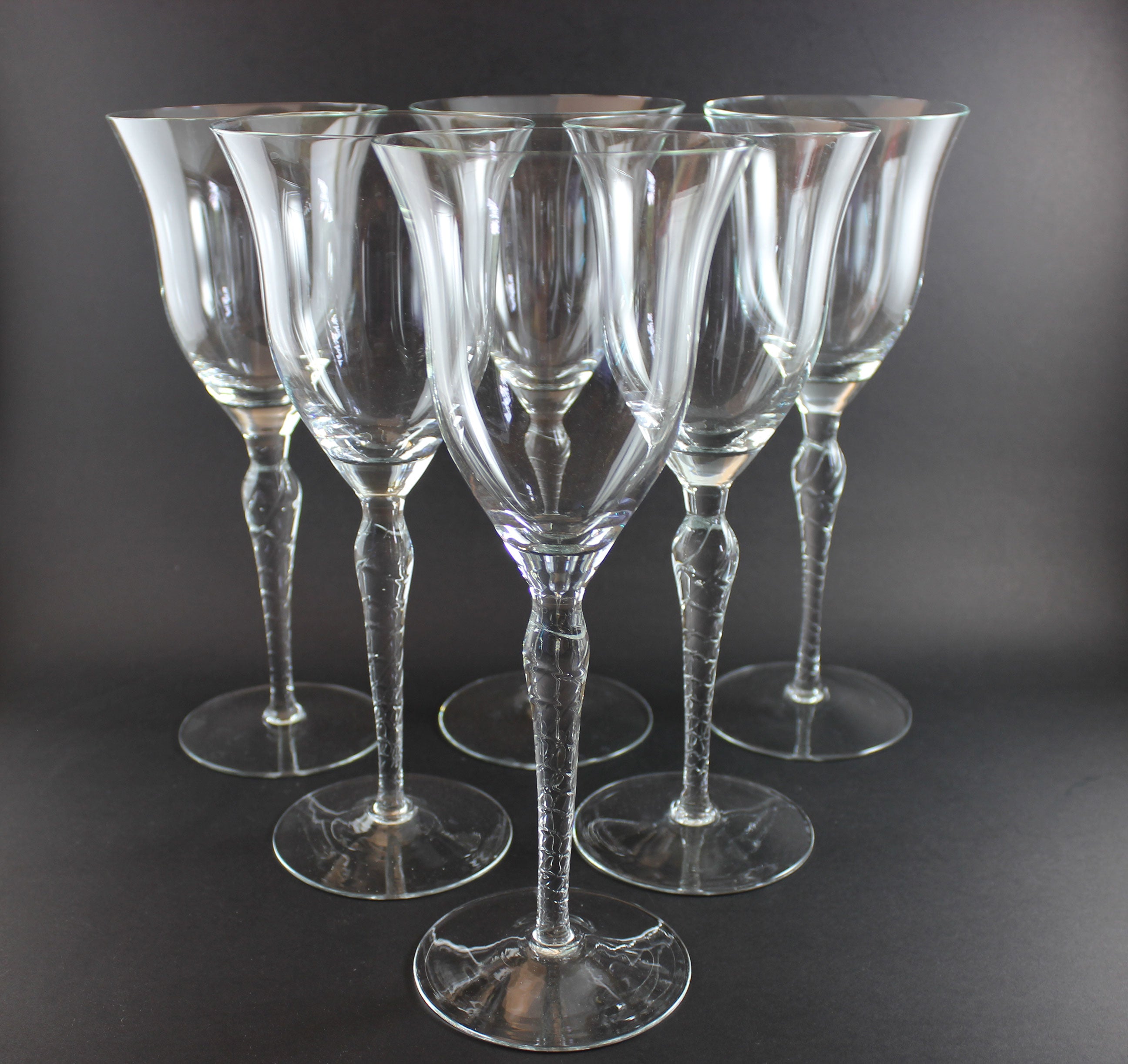 Set of six clear wine glasses with textured stems on a dark background