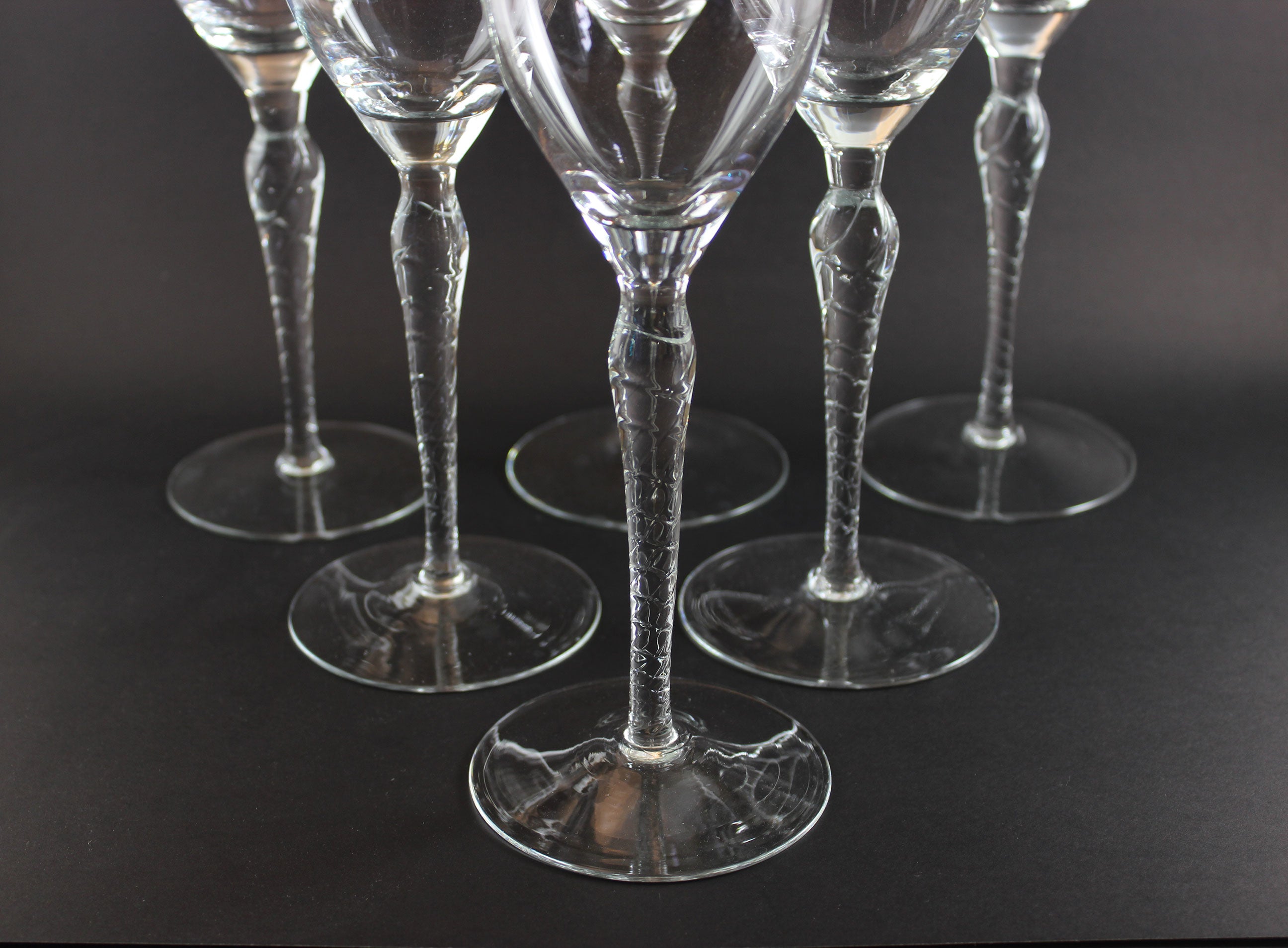 Set of six clear wine glasses with textured stems on a black background