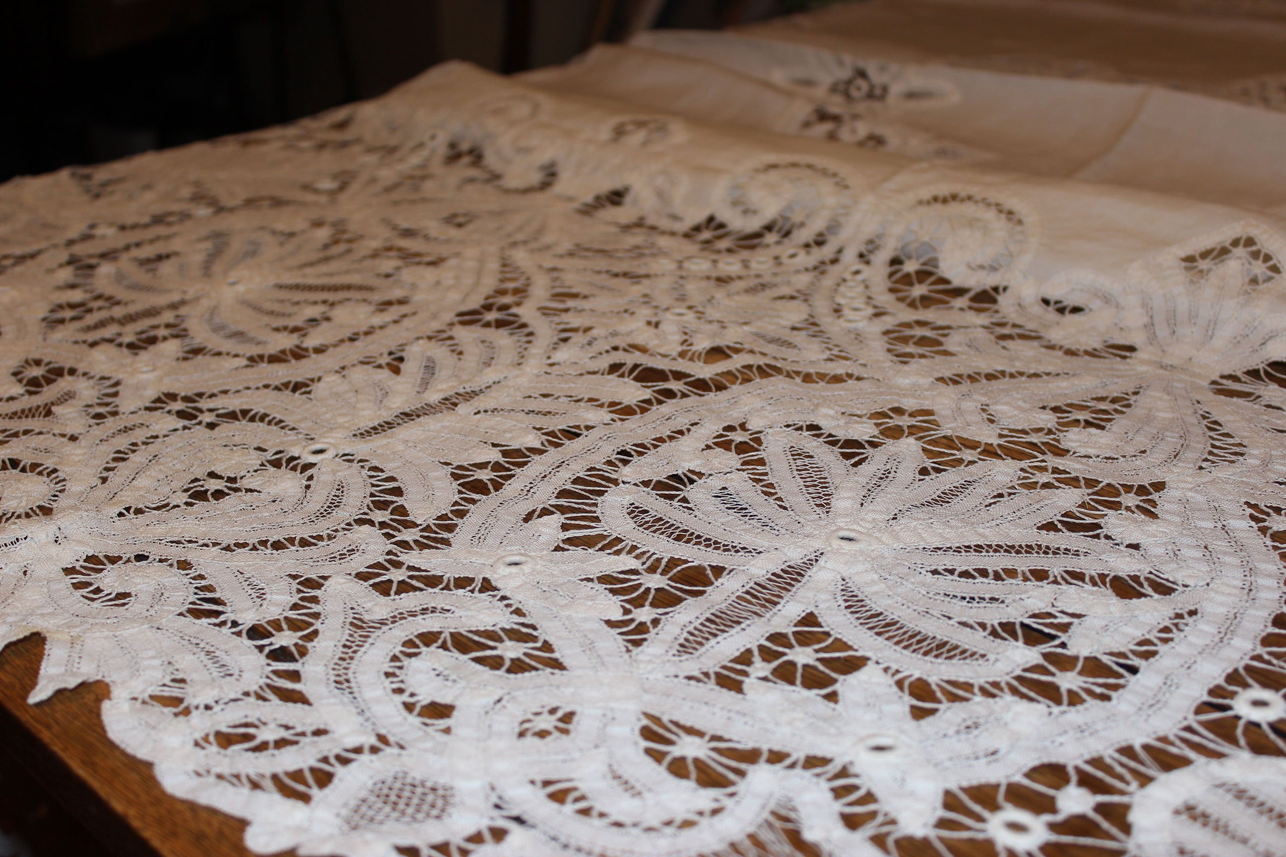Close-up of a lace tablecloth with intricate patterns on a wooden surface.