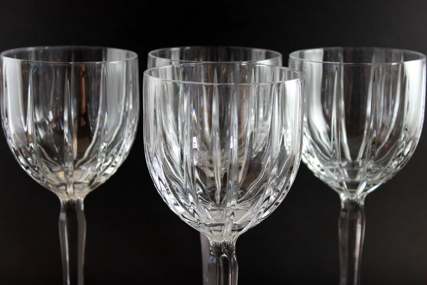 Set of four clear glass wine glasses on a black background
