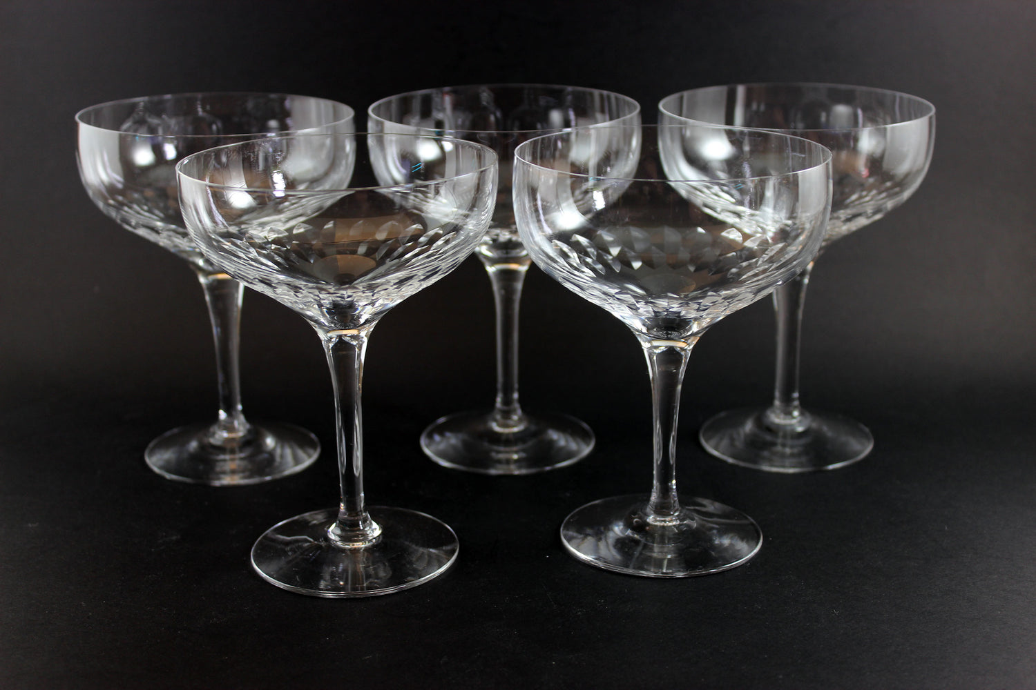 Set of six clear champagne coupe glasses on a black background