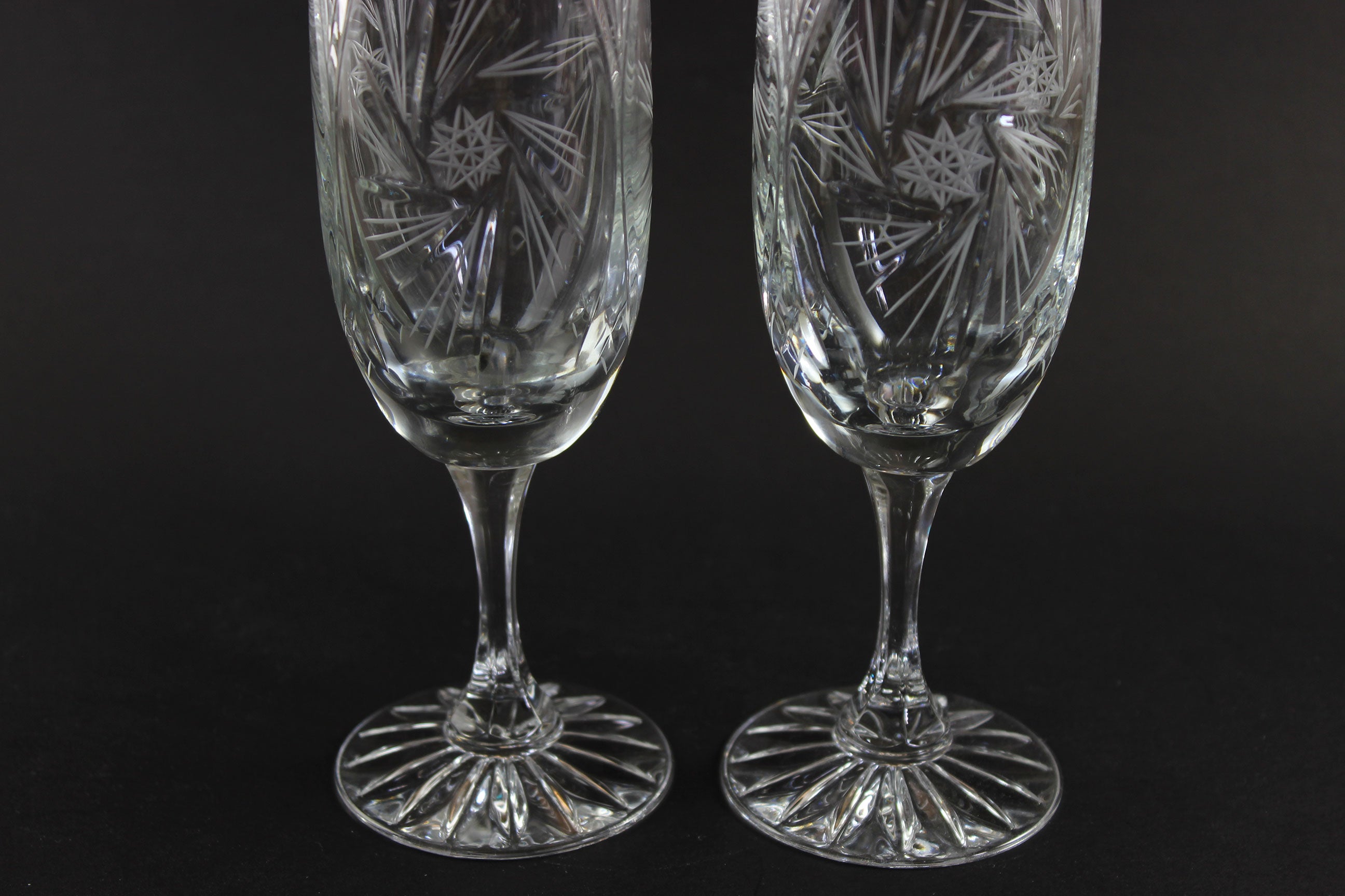 Two crystal champagne flutes with cut pinwheel design on a black background
