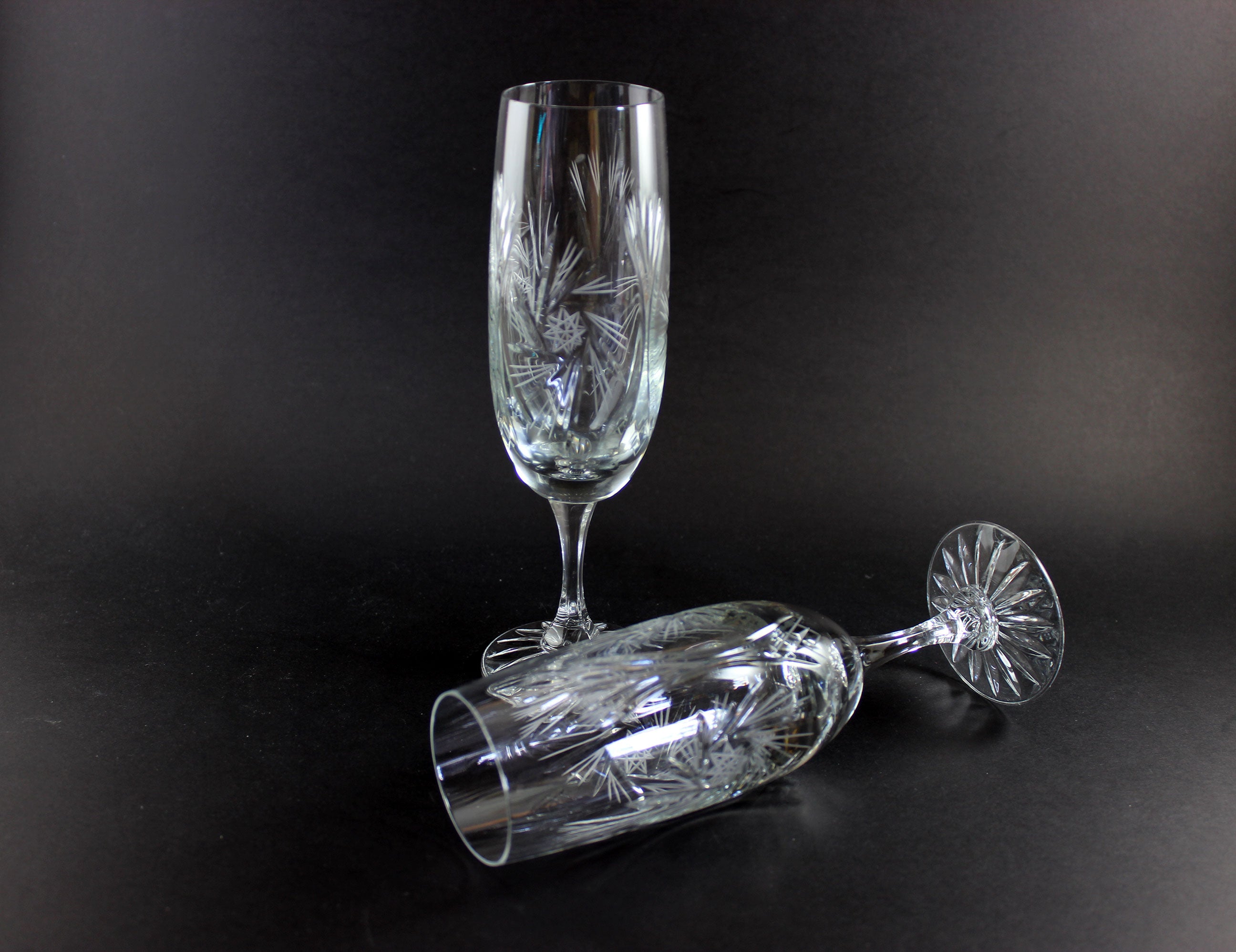Two crystal champagne flutes with cut pinwheel design on a black background