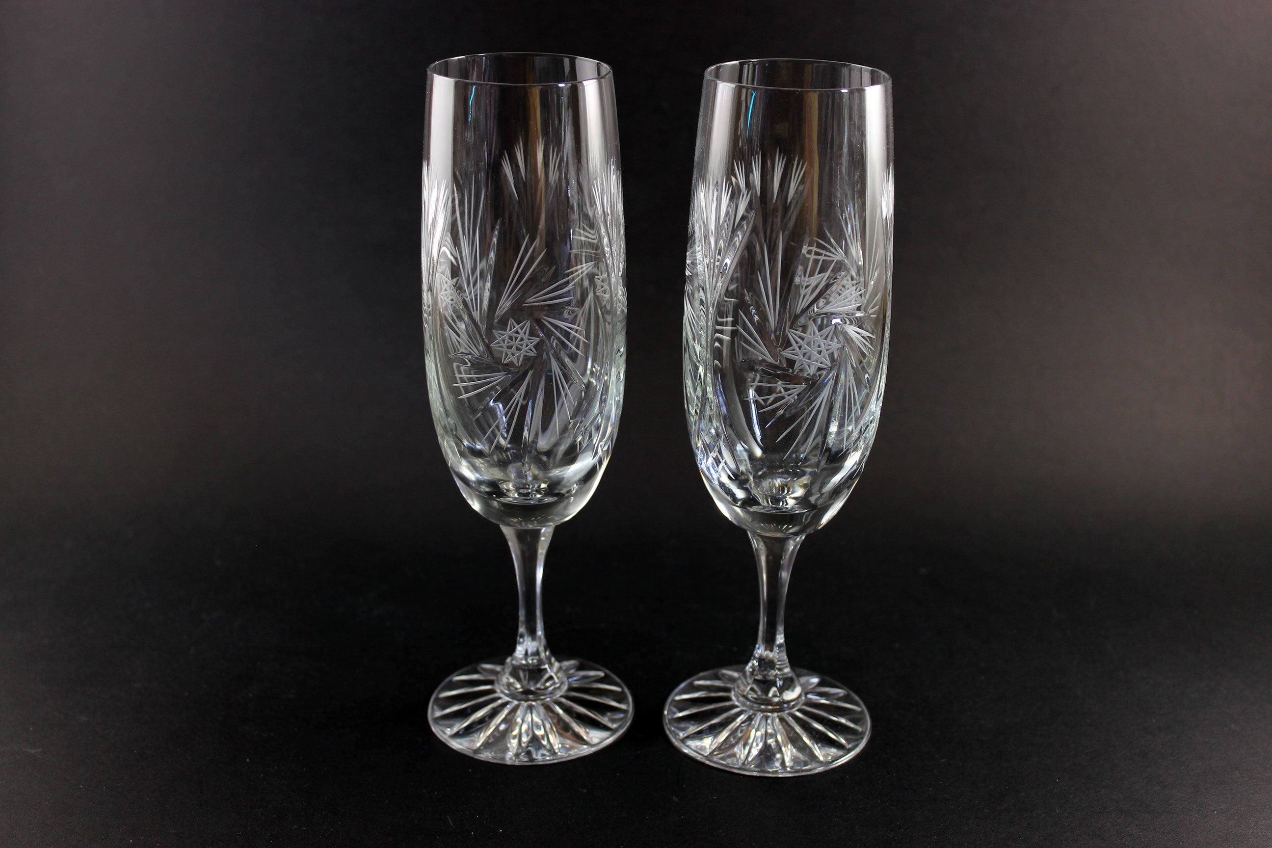 Two crystal champagne flutes with cut pinwheel design on a black background