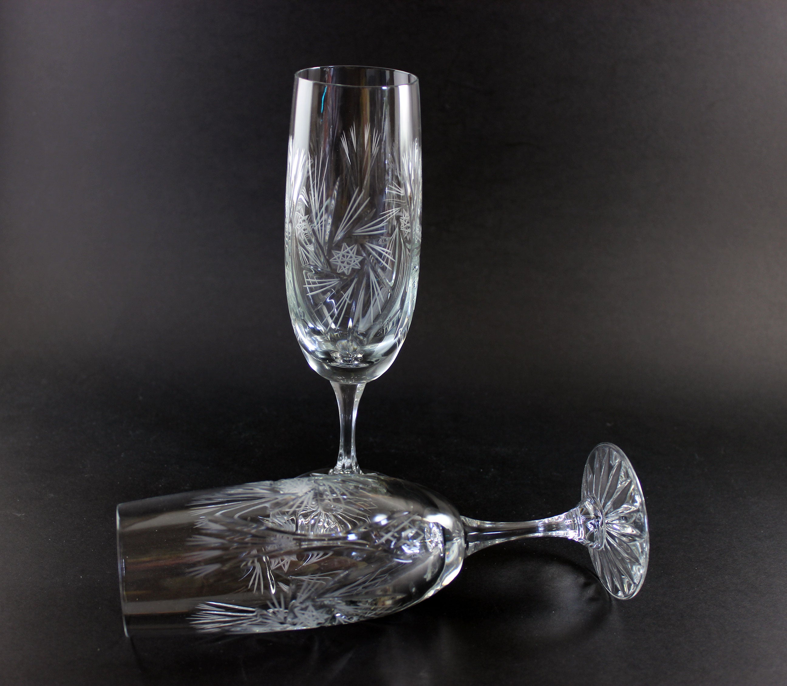 Two crystal champagne flutes with cut pinwheel design on a black background