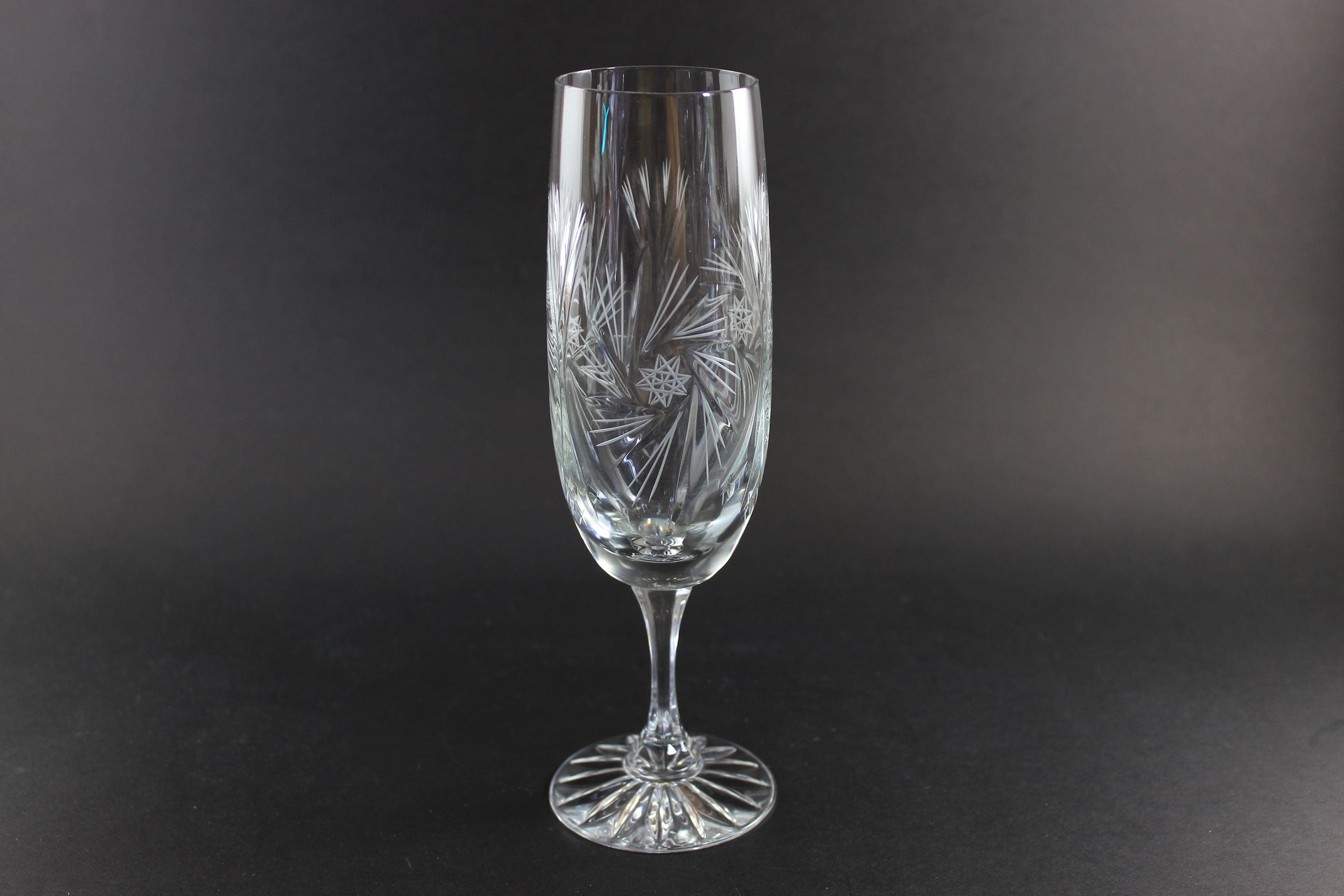Two crystal champagne flutes with cut pinwheel design on a black background