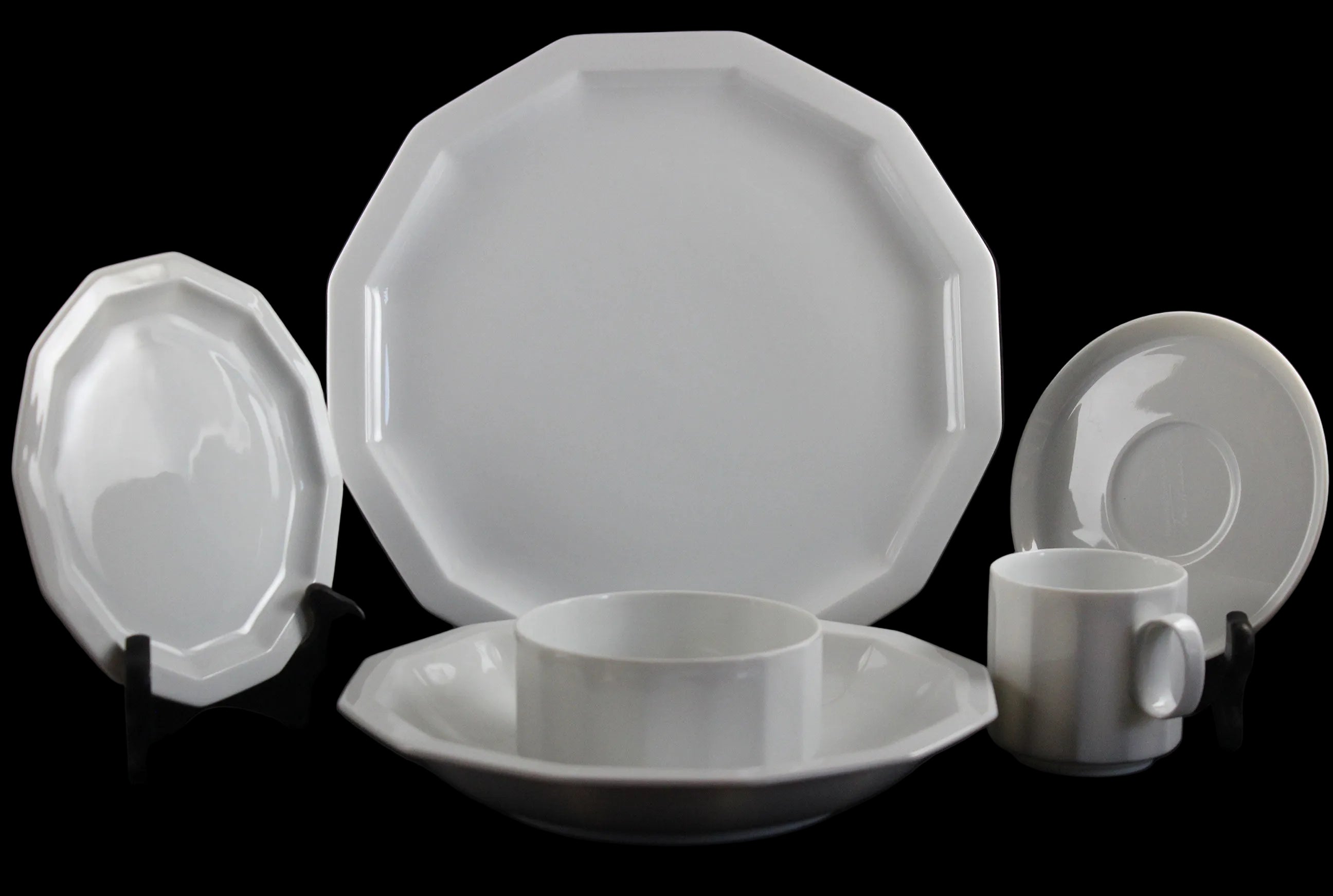 Six piece white porcelain dinnerware including plates, bowls, cup and saucer on a black background
