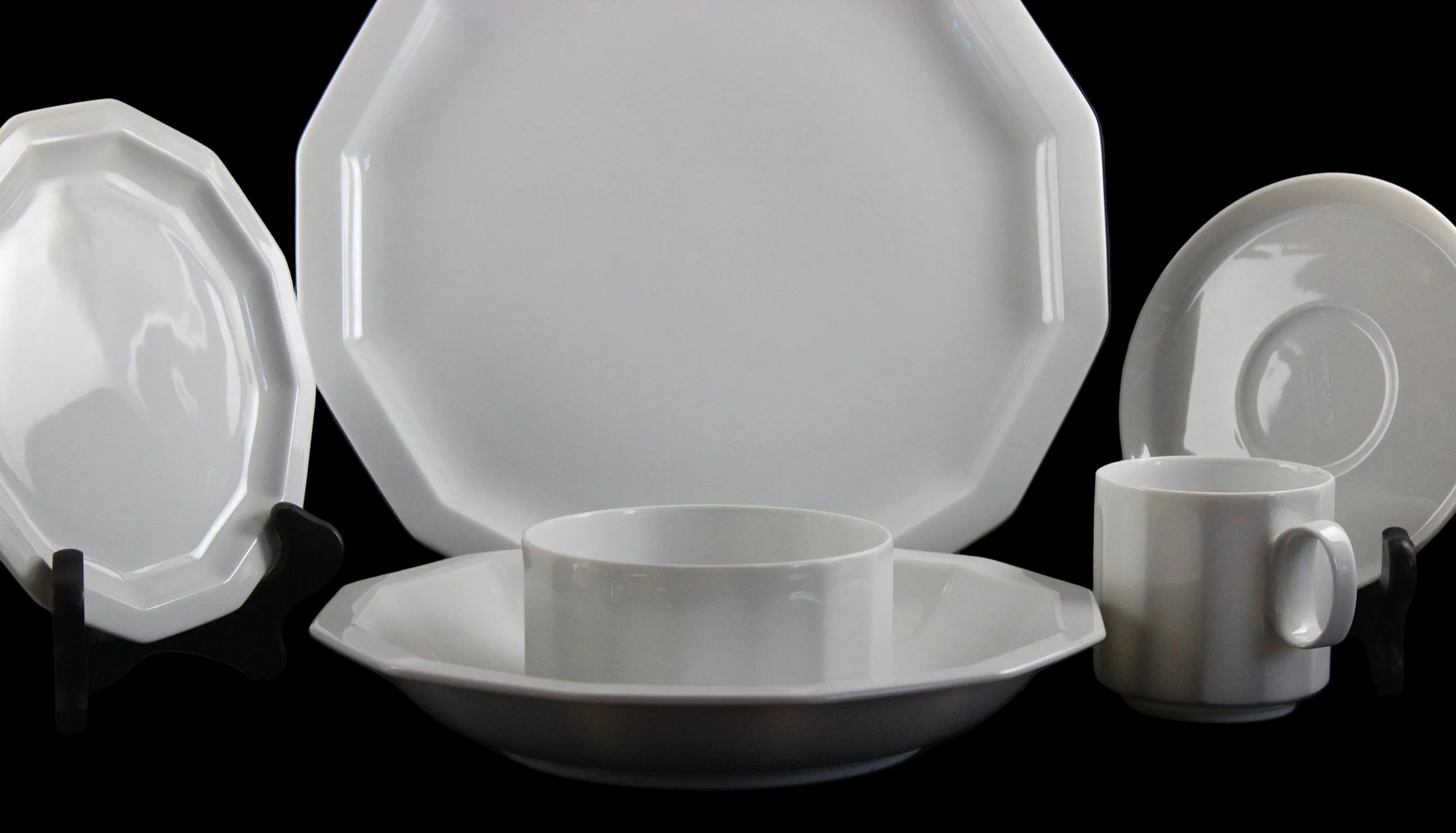 Six piece white porcelain dinnerware including plates, bowls, cup and saucer on a black background