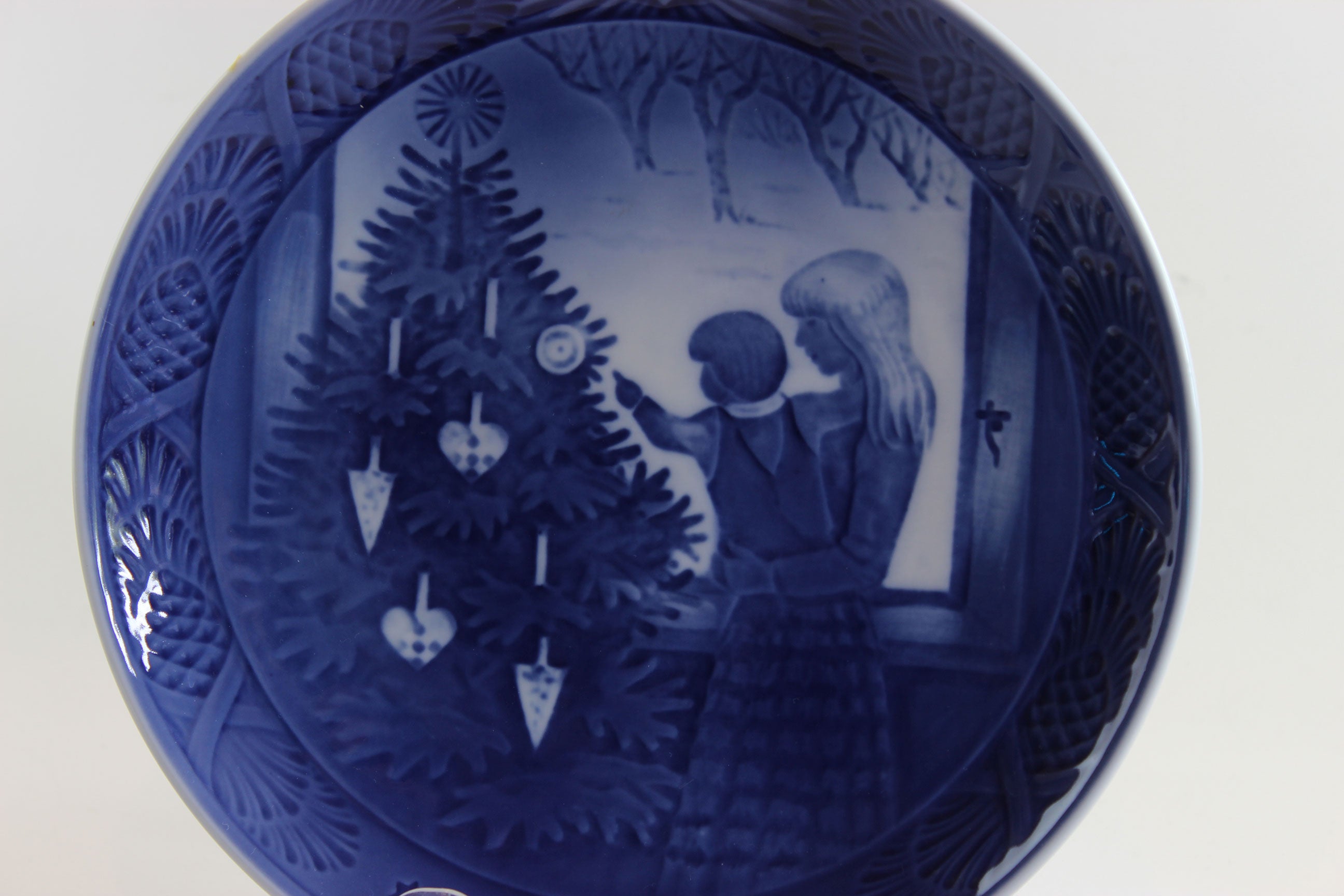 Decorative blue plate with a Christmas scene of a mother and child admiring a Christmas tree.