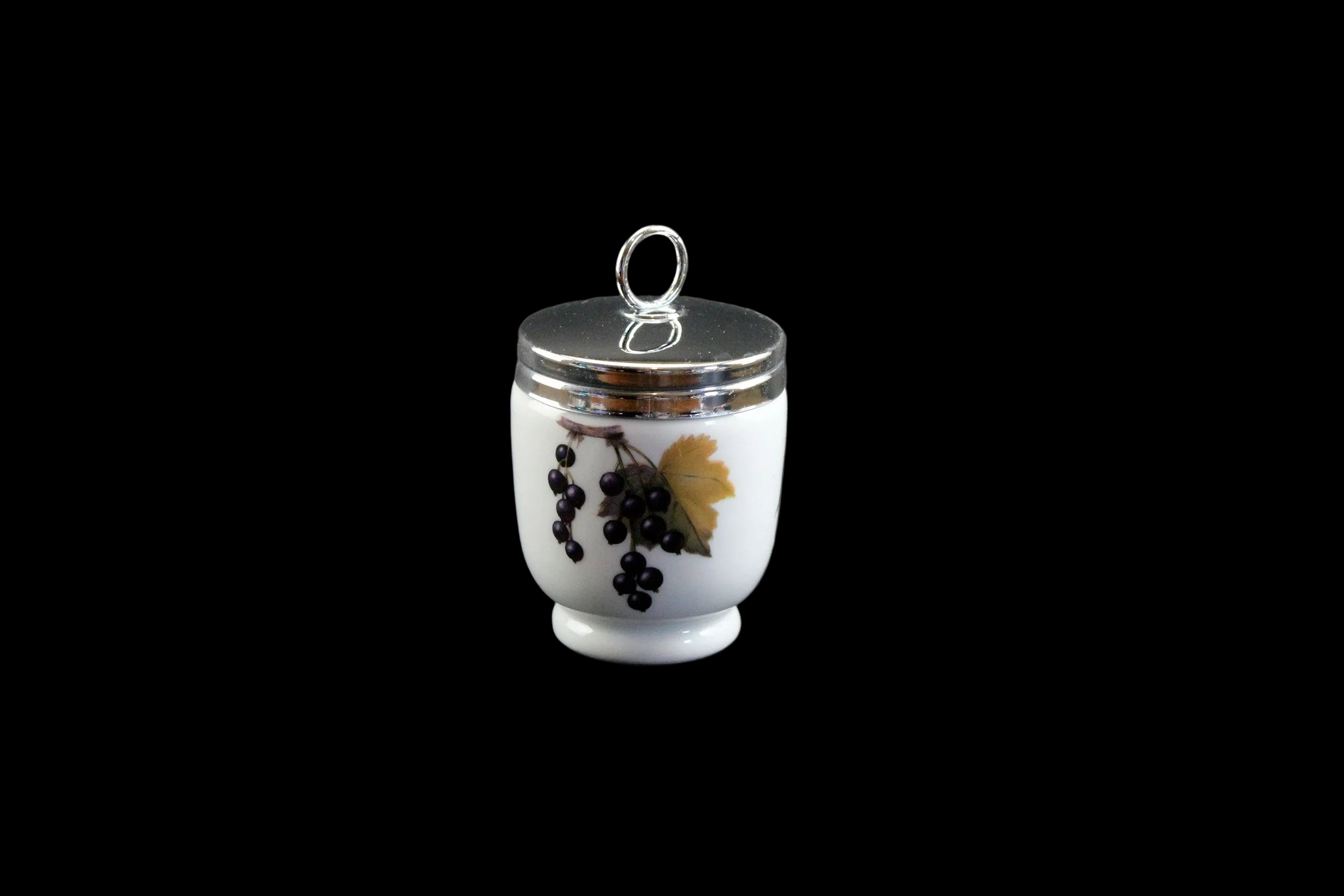 Small white ceramic container with silver lid featuring black grapes and a yellow leaf on a dark gray background