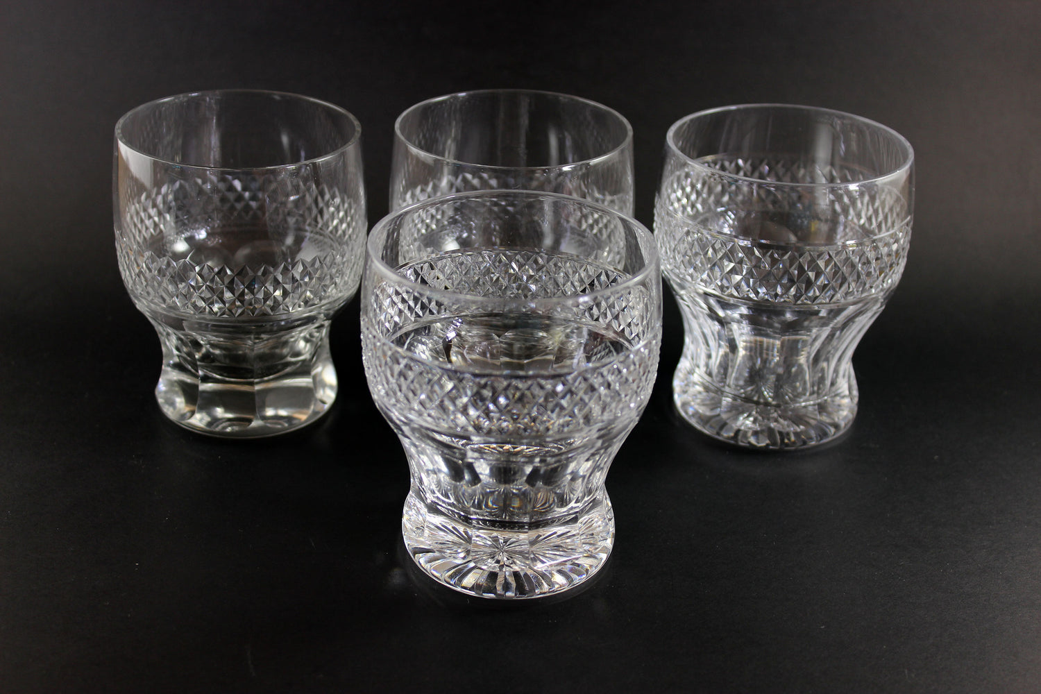 Set of four clear glass tumblers with textured design on a black background