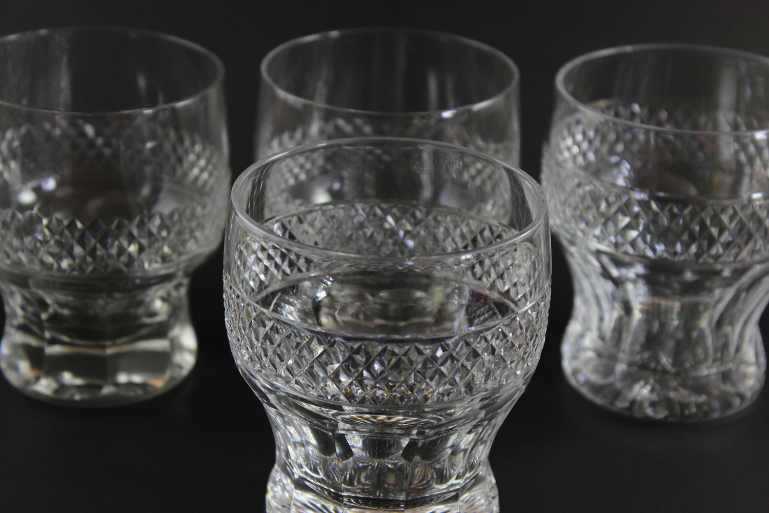 Set of four crystal glasses with intricate patterns on a black background