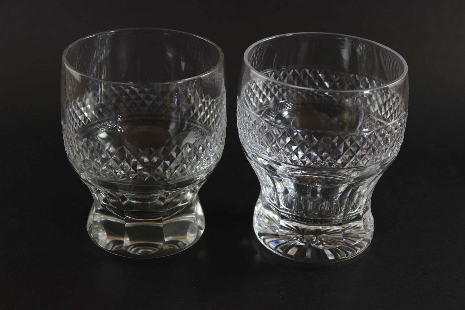 Two crystal glasses with diamond cut pattern on a black background
