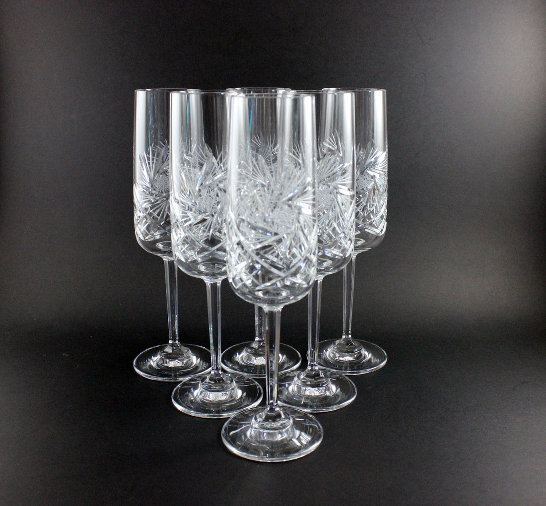 Set of six crystal champagne flutes with cut designs on a black background
