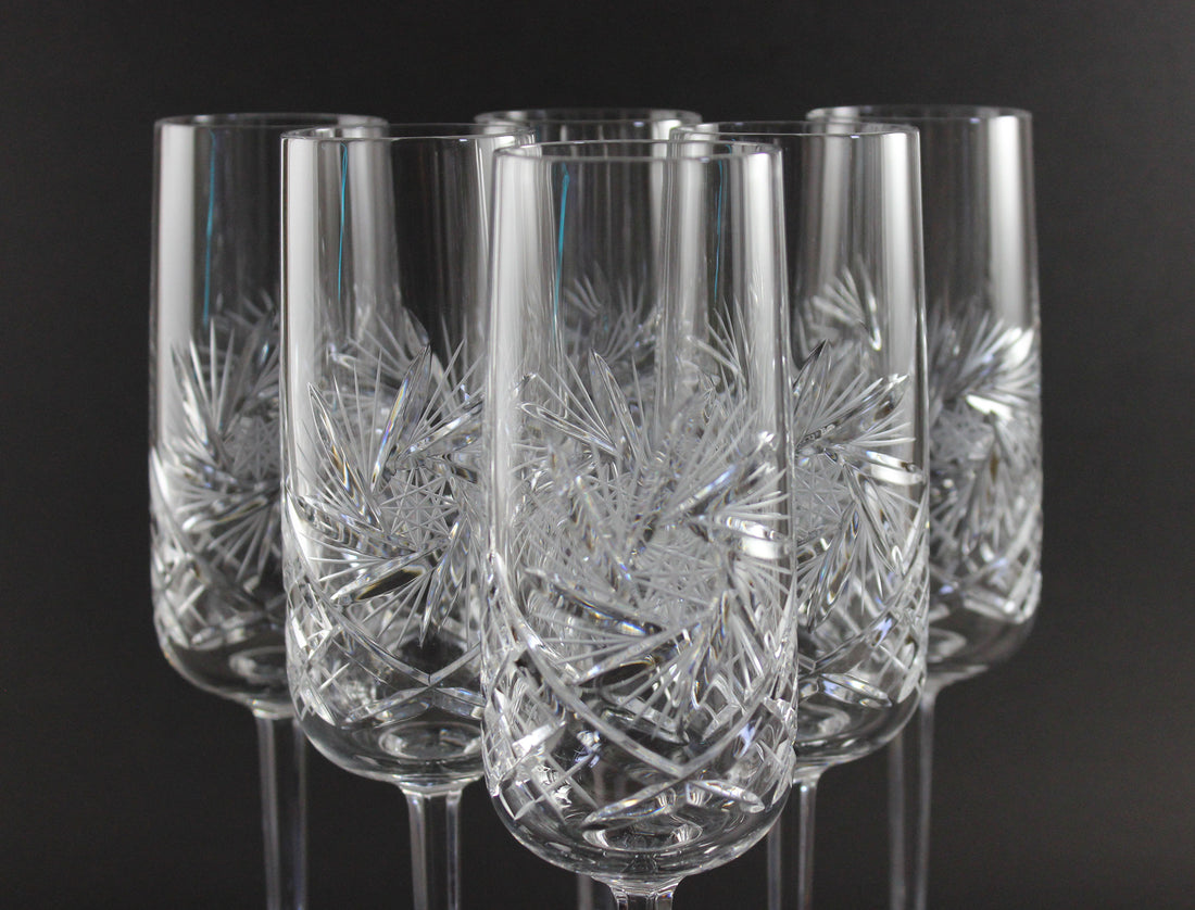 Set of six crystal champagne flutes with cut designs on a black background