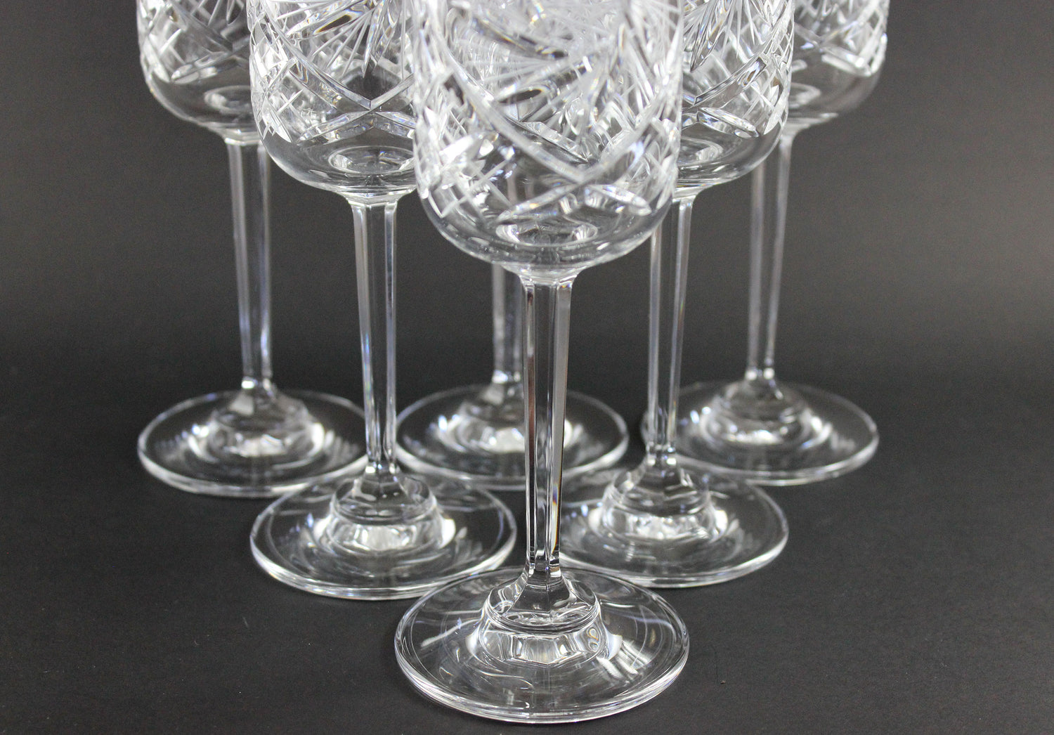 Set of six crystal champagne flutes with cut designs on a black background