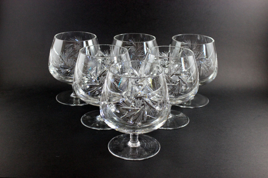 Set of six crystal glasses with intricate designs on a black background