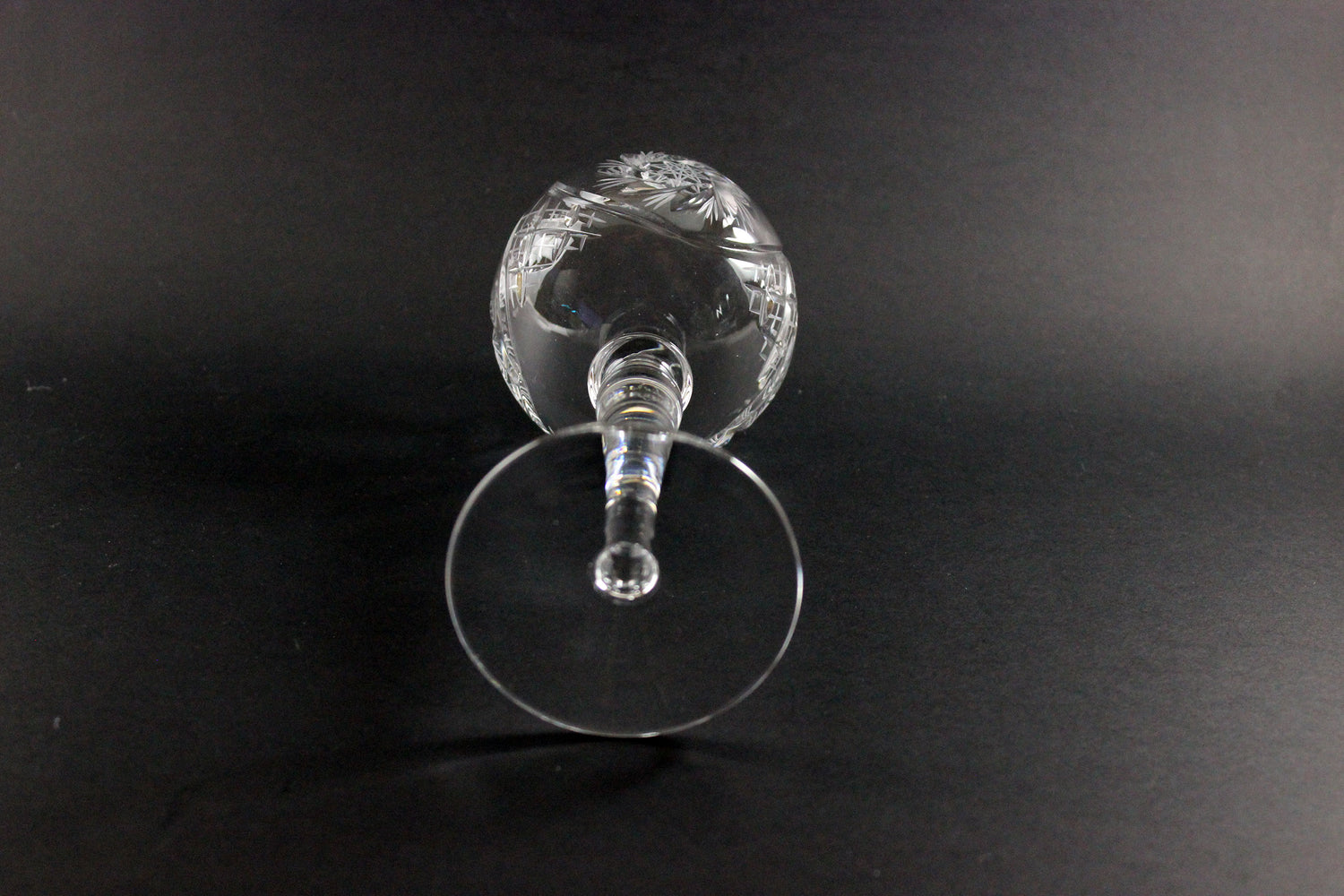 Clear glass wine goblet with intricate design on a black background
