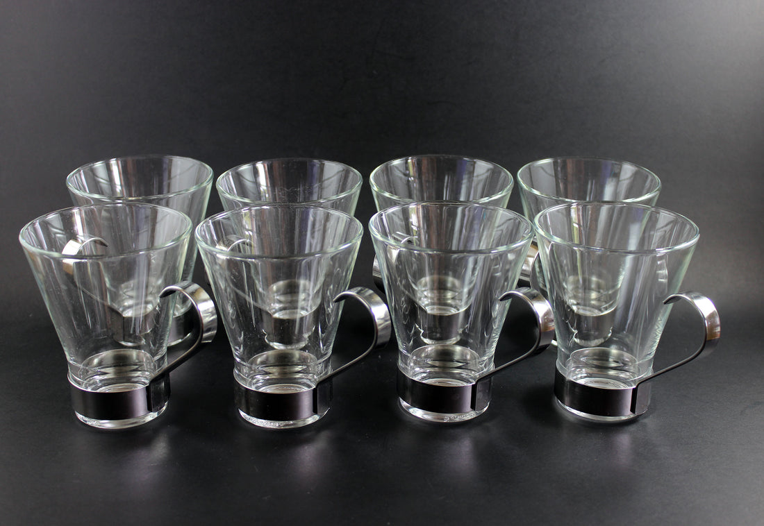 Set of clear glass tumblers with metal bases on a black background