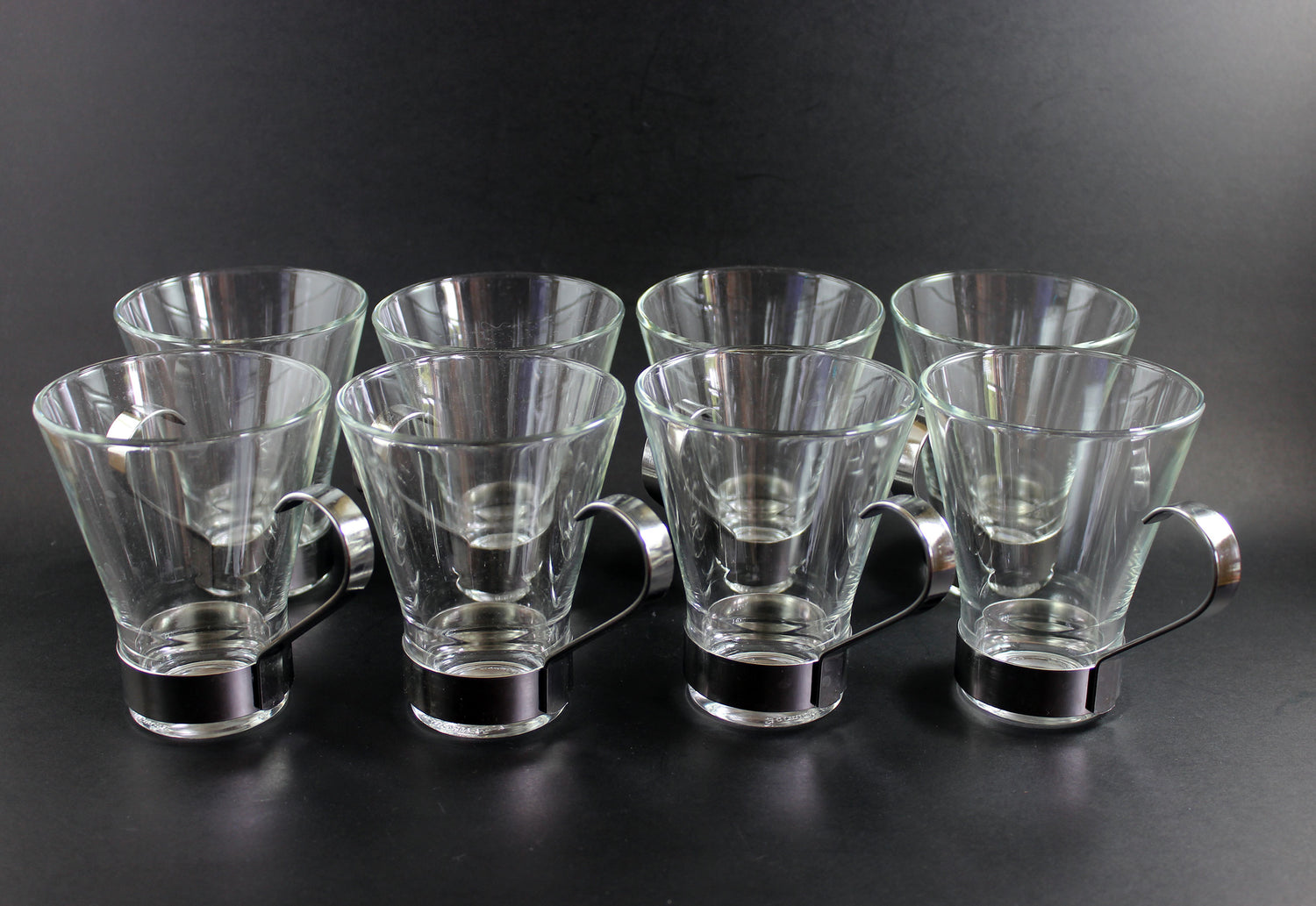 Set of clear glass tumblers with metal bases on a black background