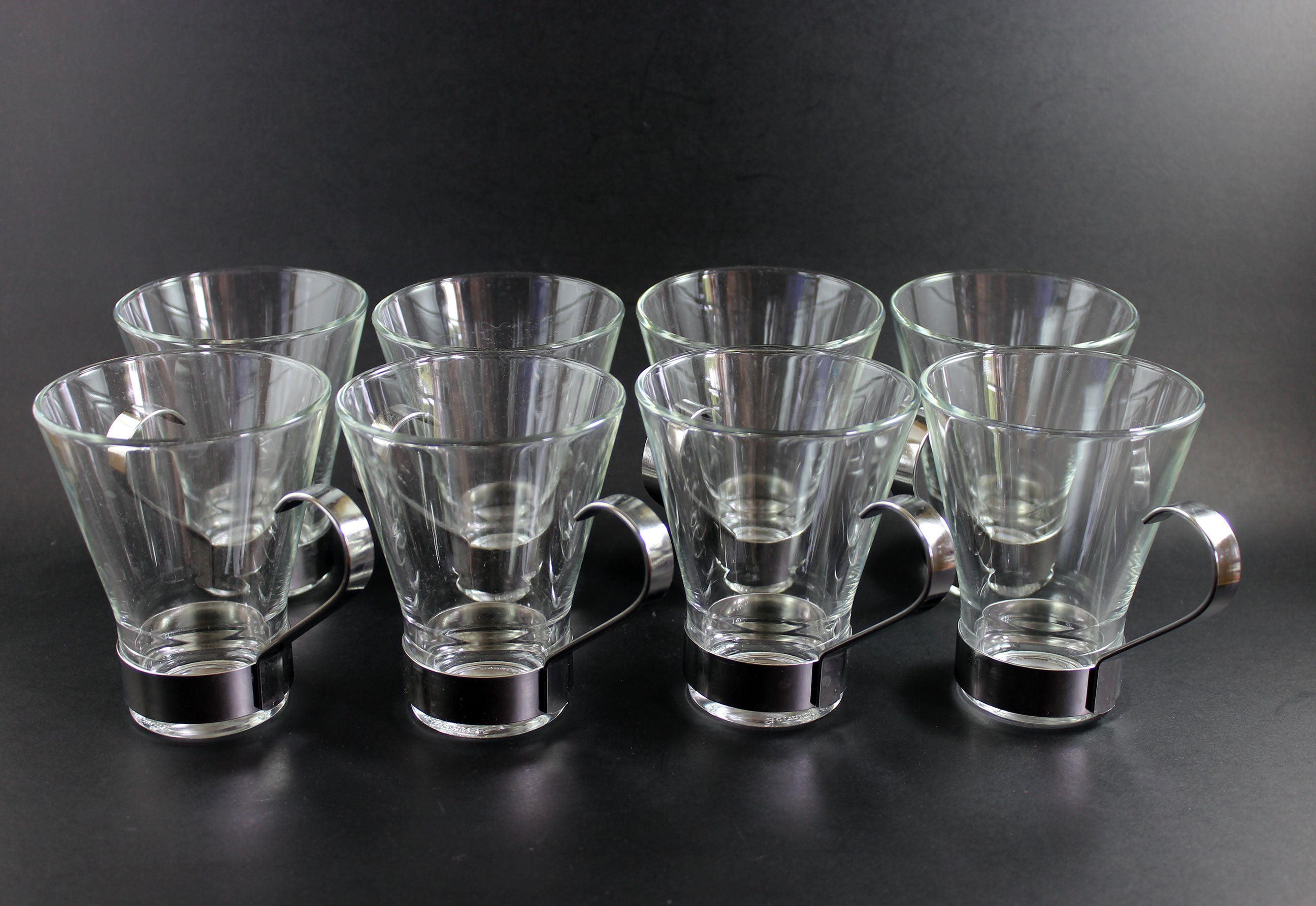 Set of clear glass tumblers with metal bases on a black background