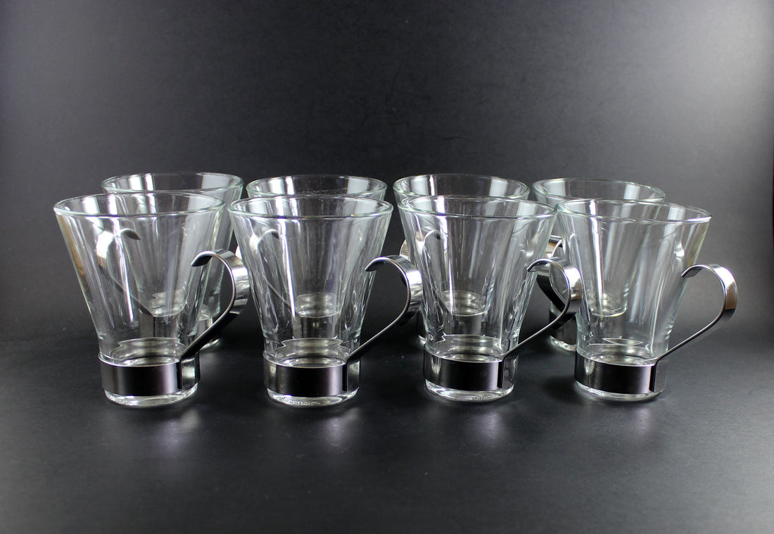 Set of six clear glass mugs with metal handles on a dark background