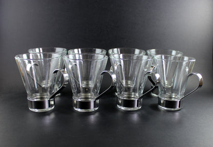 Set of six clear glass mugs with metal handles on a dark background